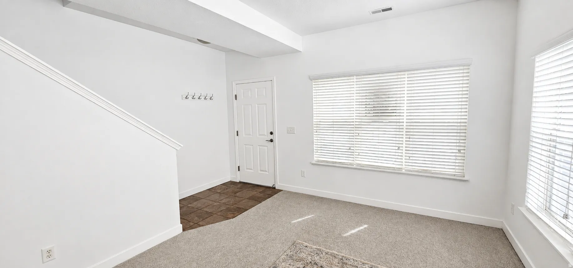 Entryway featuring tile flooring, carpeted living area, multiple windows with blinds, and white interior walls