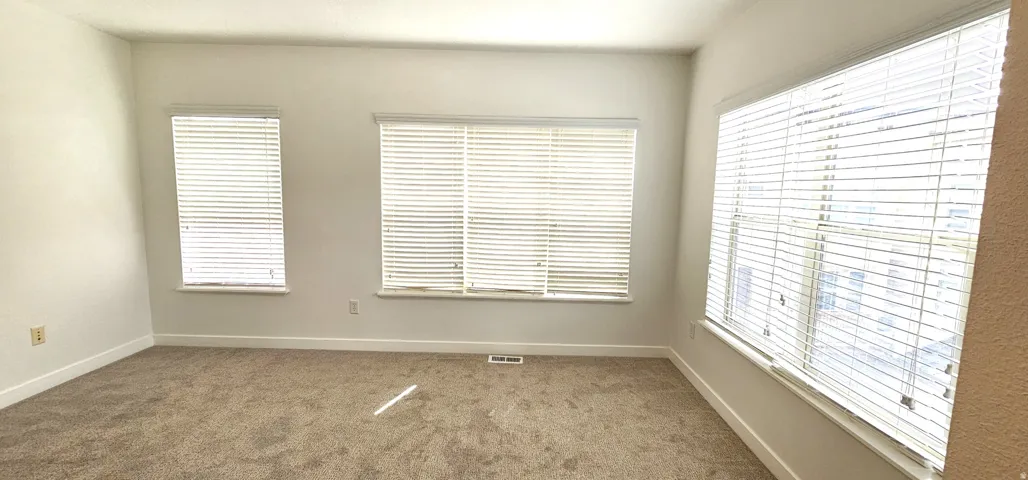 Carpeted room with multiple windows, white window blinds, and light-colored walls