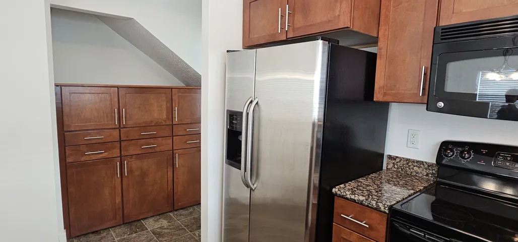 Stainless steel side-by-side refrigerator, extensive wood-finish cabinetry with brushed nickel hardware, built-in microwave, and stone-finish countertops