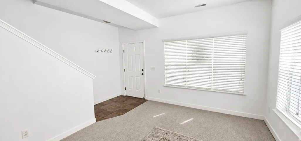 Entryway featuring tile flooring, carpeted living area, multiple windows with blinds, and white interior walls