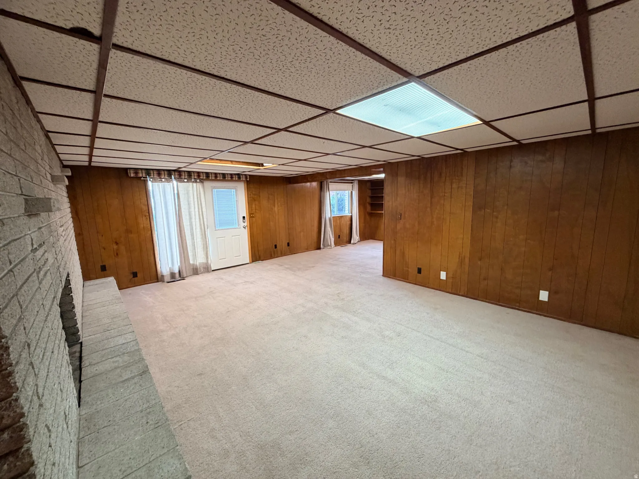 Basement featuring a paneled ceiling, light colored carpet, a fireplace, and wooden walls