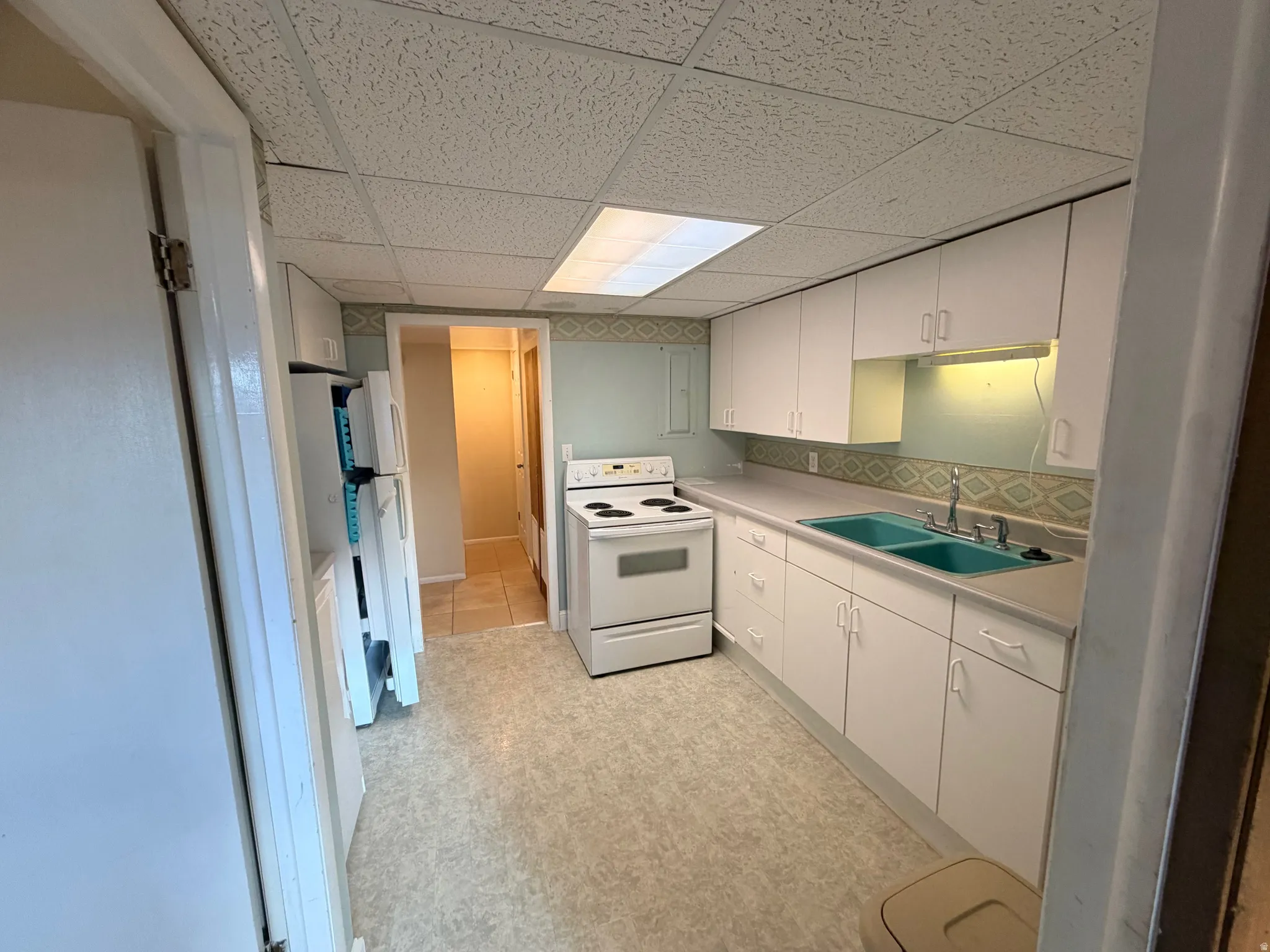 Kitchen featuring white appliances, light countertops, a paneled ceiling, white cabinetry, and tasteful backsplash