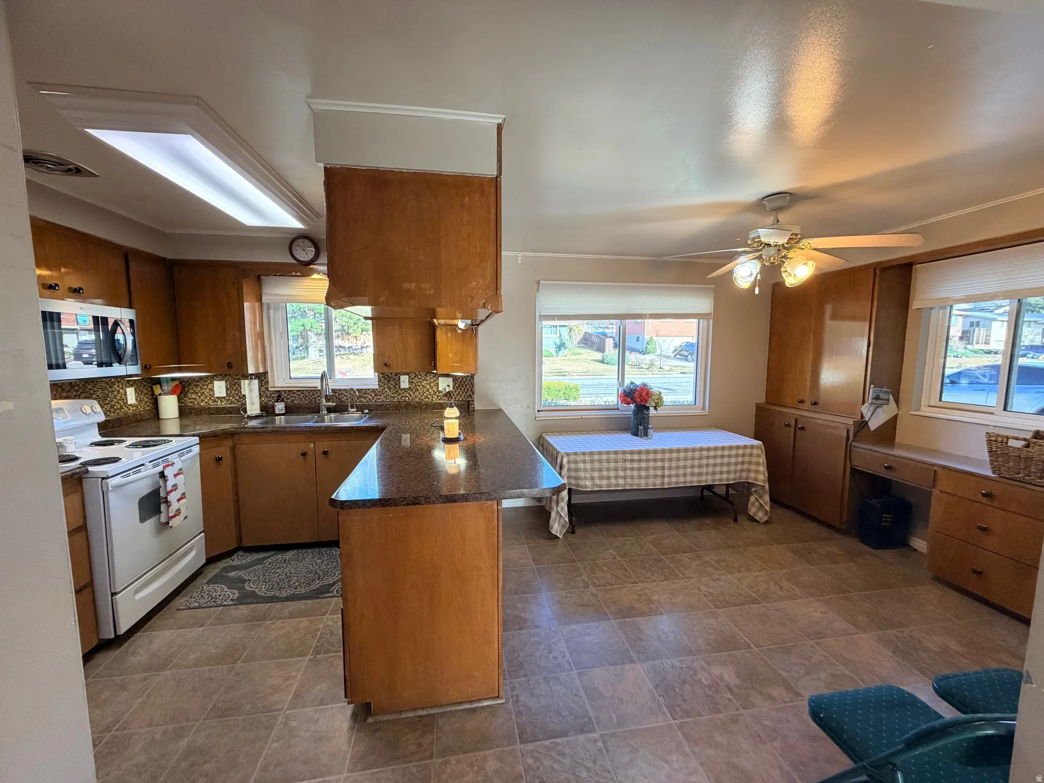 Kitchen featuring a peninsula, wood finish cabinetry, white electric stove, stainless steel microwave, and a ceiling fan