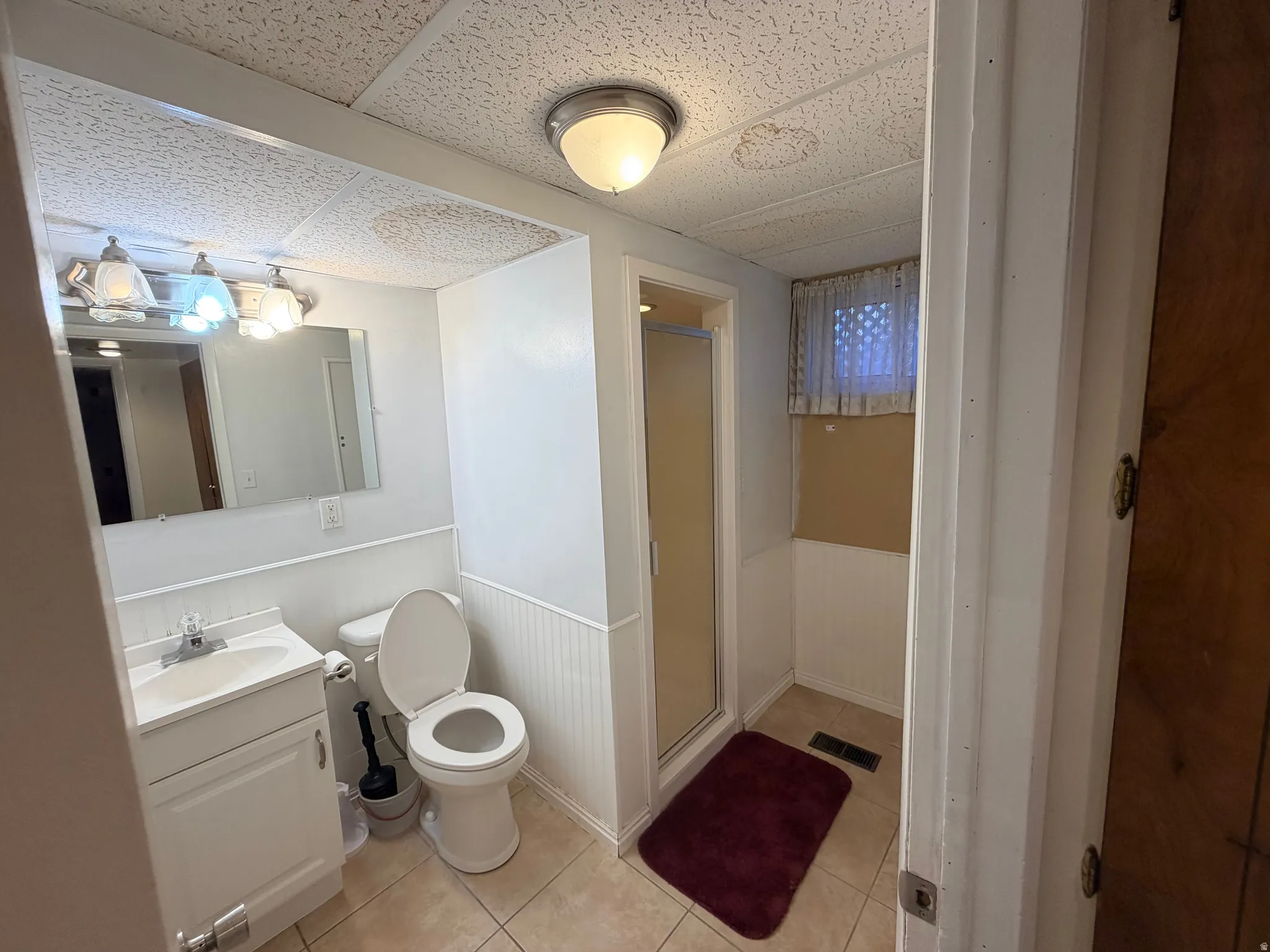 Bathroom featuring a wainscoted wall, vanity, a stall shower, a paneled ceiling, and light tile patterned floors