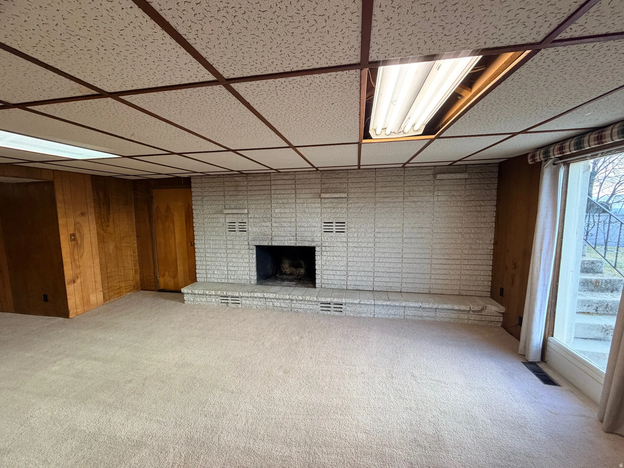 Below grade area featuring carpet floors, a drop ceiling, wooden walls, and a fireplace
