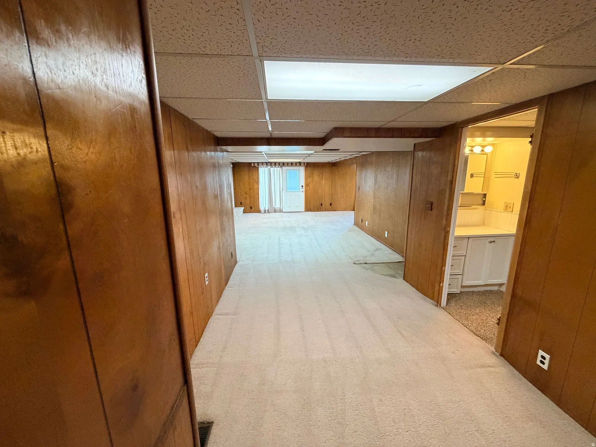 Corridor featuring wooden walls, light carpet, and a drop ceiling