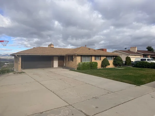 Single story home featuring brick siding, an attached garage, driveway, a chimney, and a front lawn