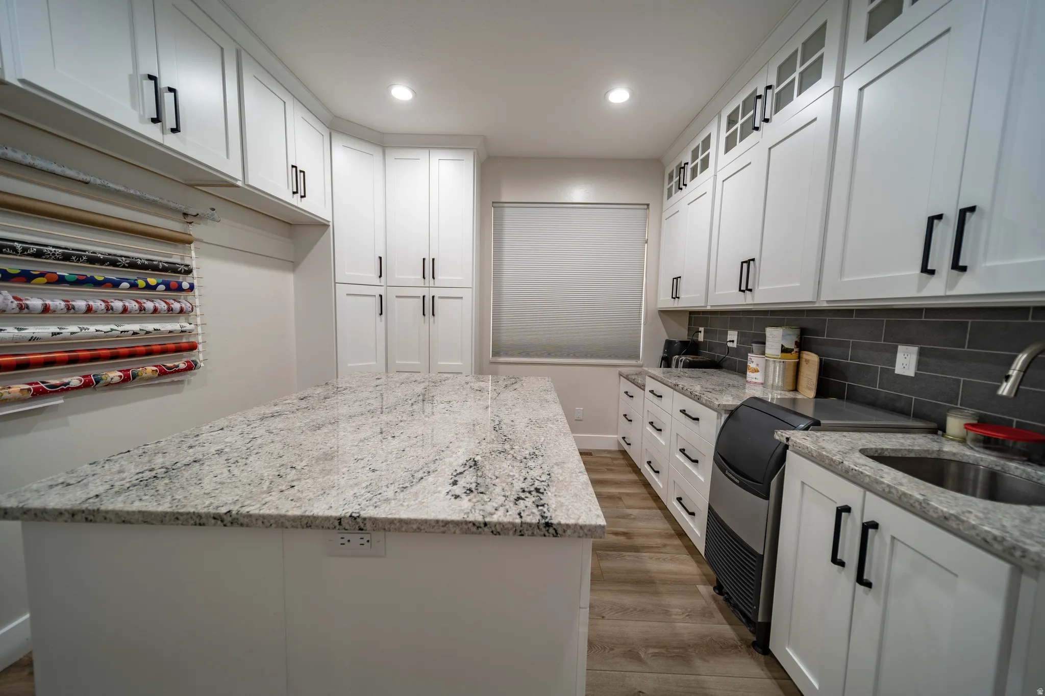 Kitchen with light wood-style flooring, light stone countertops, white cabinets, a kitchen island, and recessed lighting