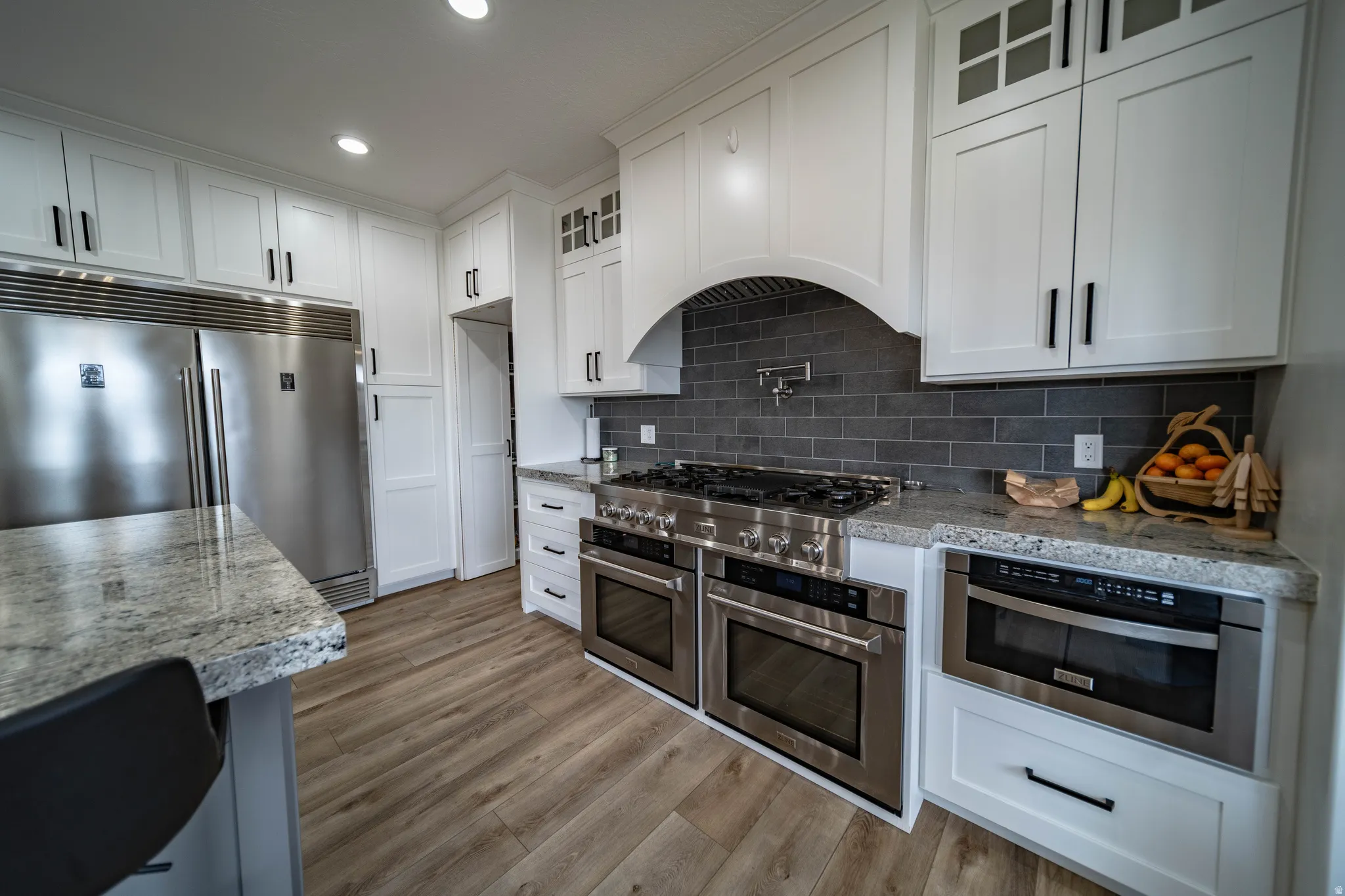 Kitchen with built in appliances, light stone counters, white cabinetry, glass fronted cabinets, and recessed lighting