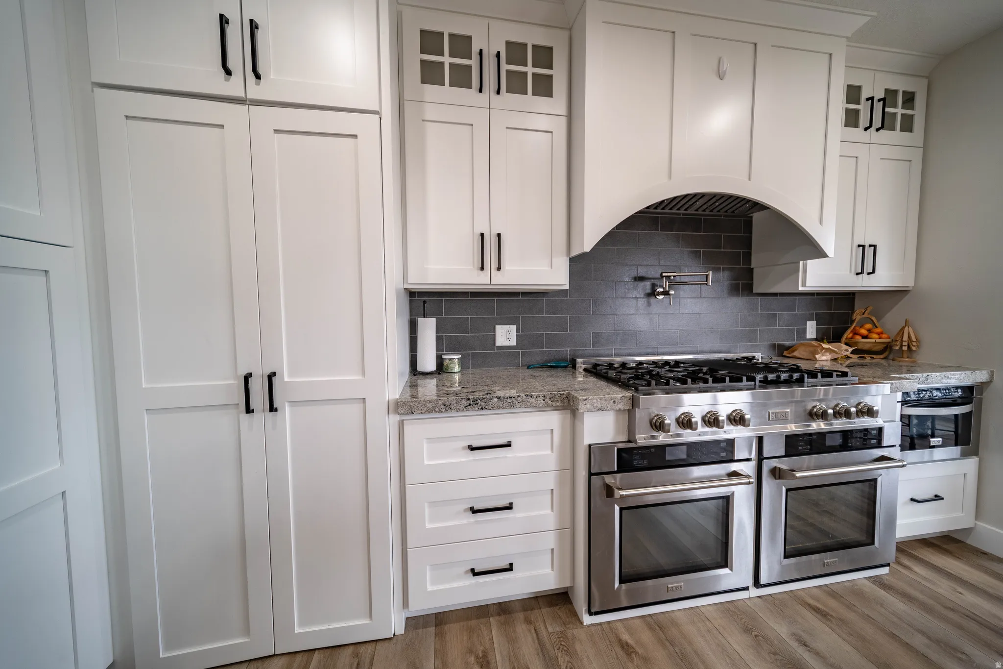 Kitchen with light stone counters, white cabinets, glass fronted cabinets, light wood-type flooring, and stainless steel appliances