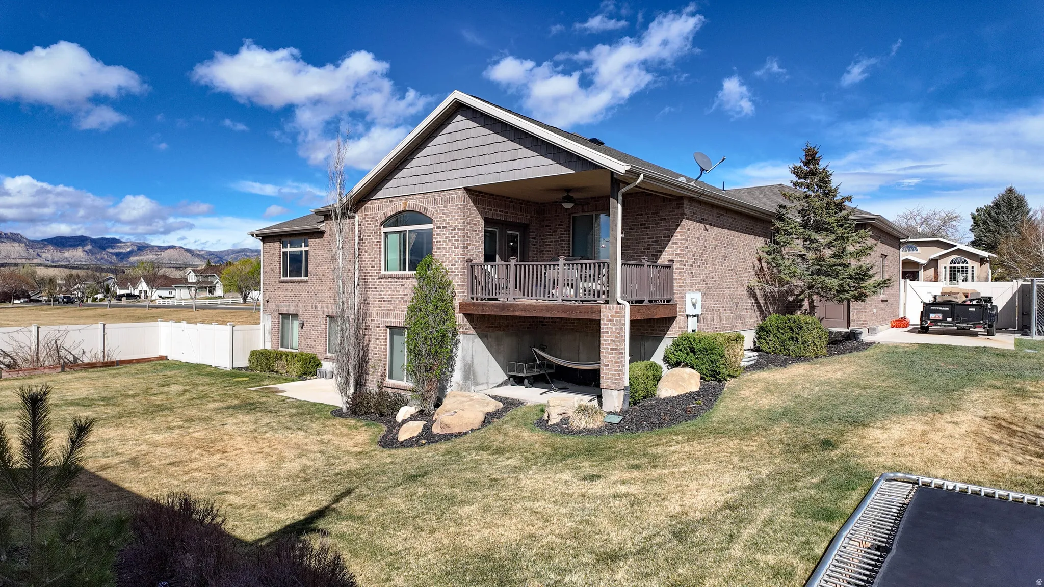 Back of house with a fenced backyard, a balcony, brick siding, a ceiling fan, and a patio