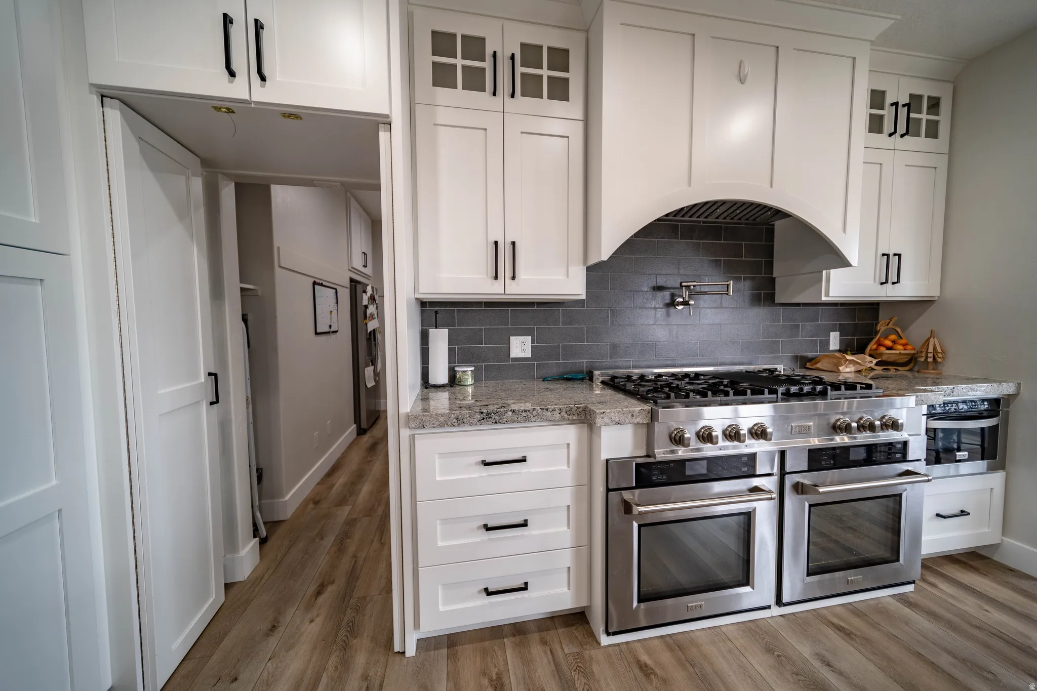 Kitchen featuring light stone counters, white cabinets, glass fronted cabinets, and light wood-style floors