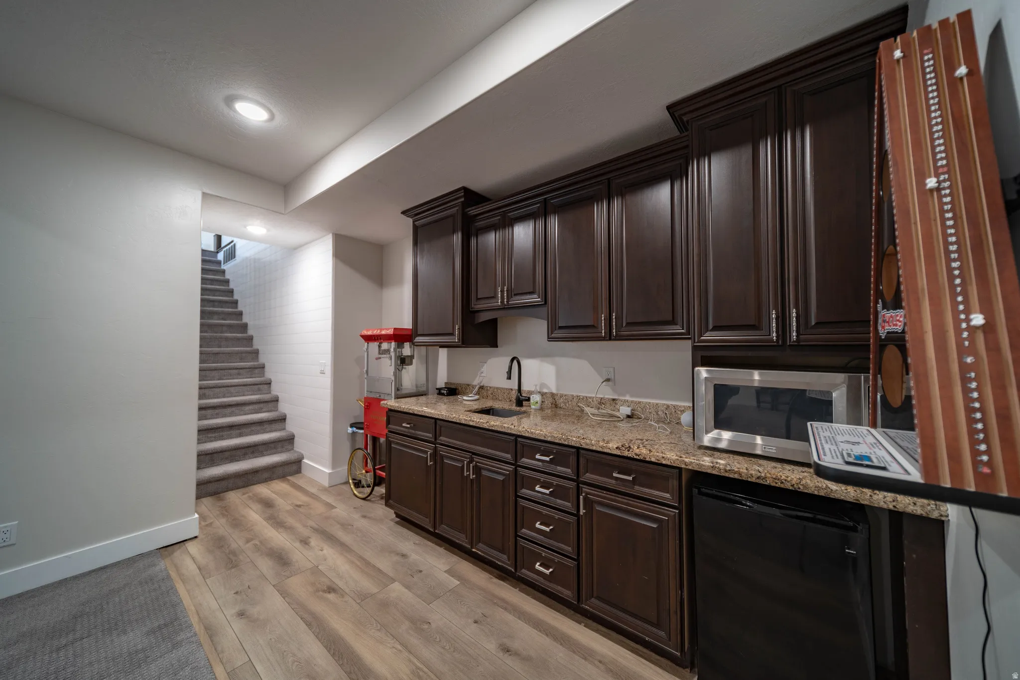 Kitchen with dark wood finish cabinets, black fridge, light wood finished floors, light stone countertops, and recessed lighting
