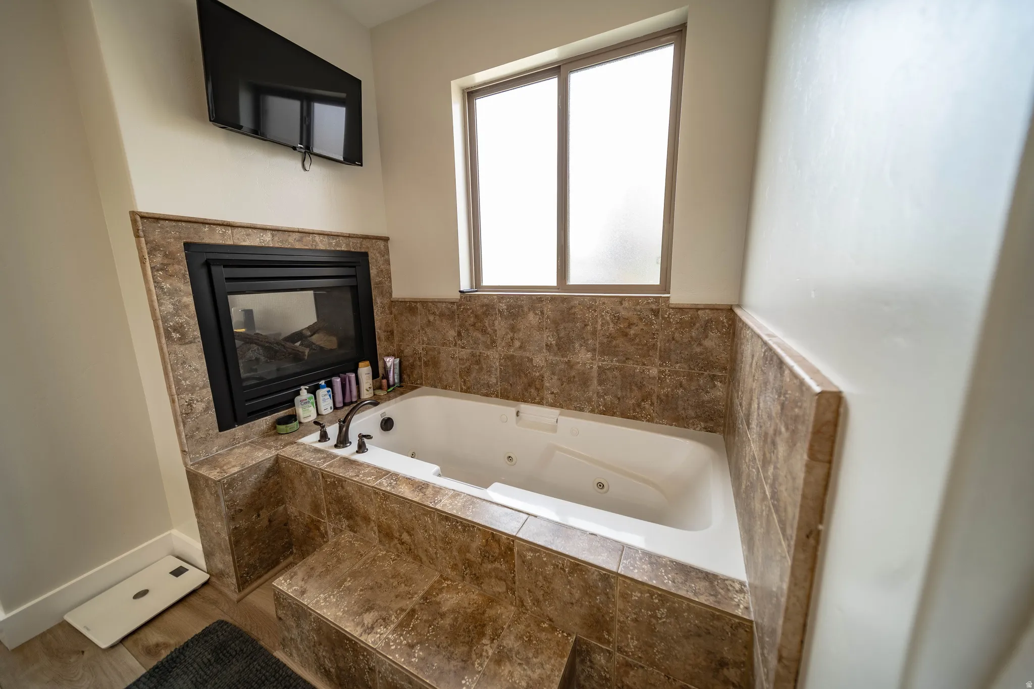 Full bath featuring a tub with jets and a glass covered fireplace