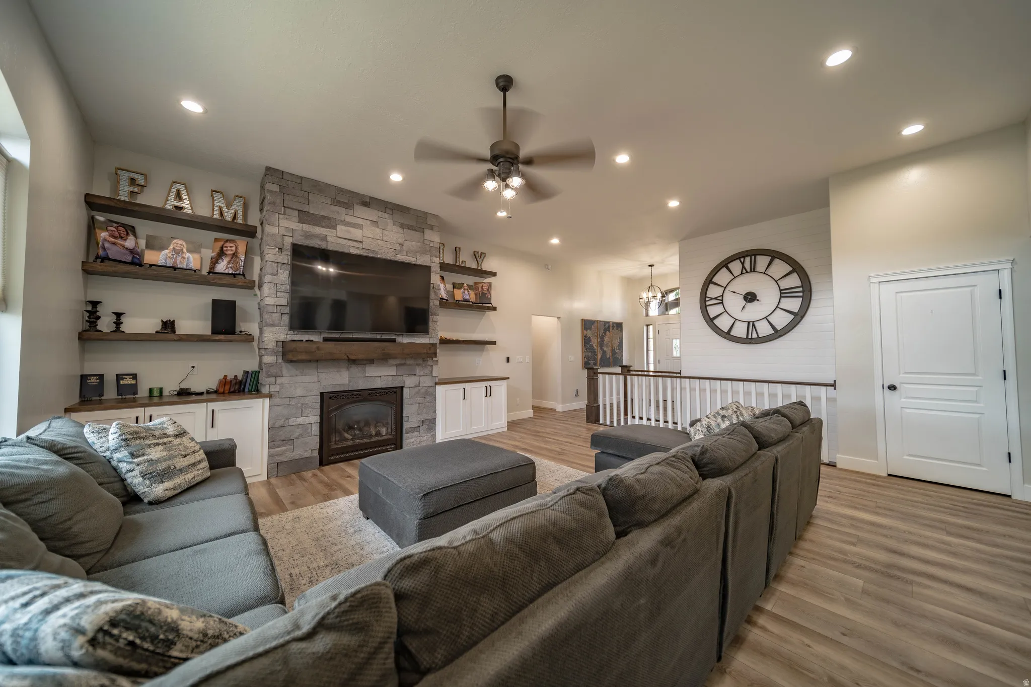Living room with light wood-type flooring, a ceiling fan, a stone fireplace, and suspended lighting