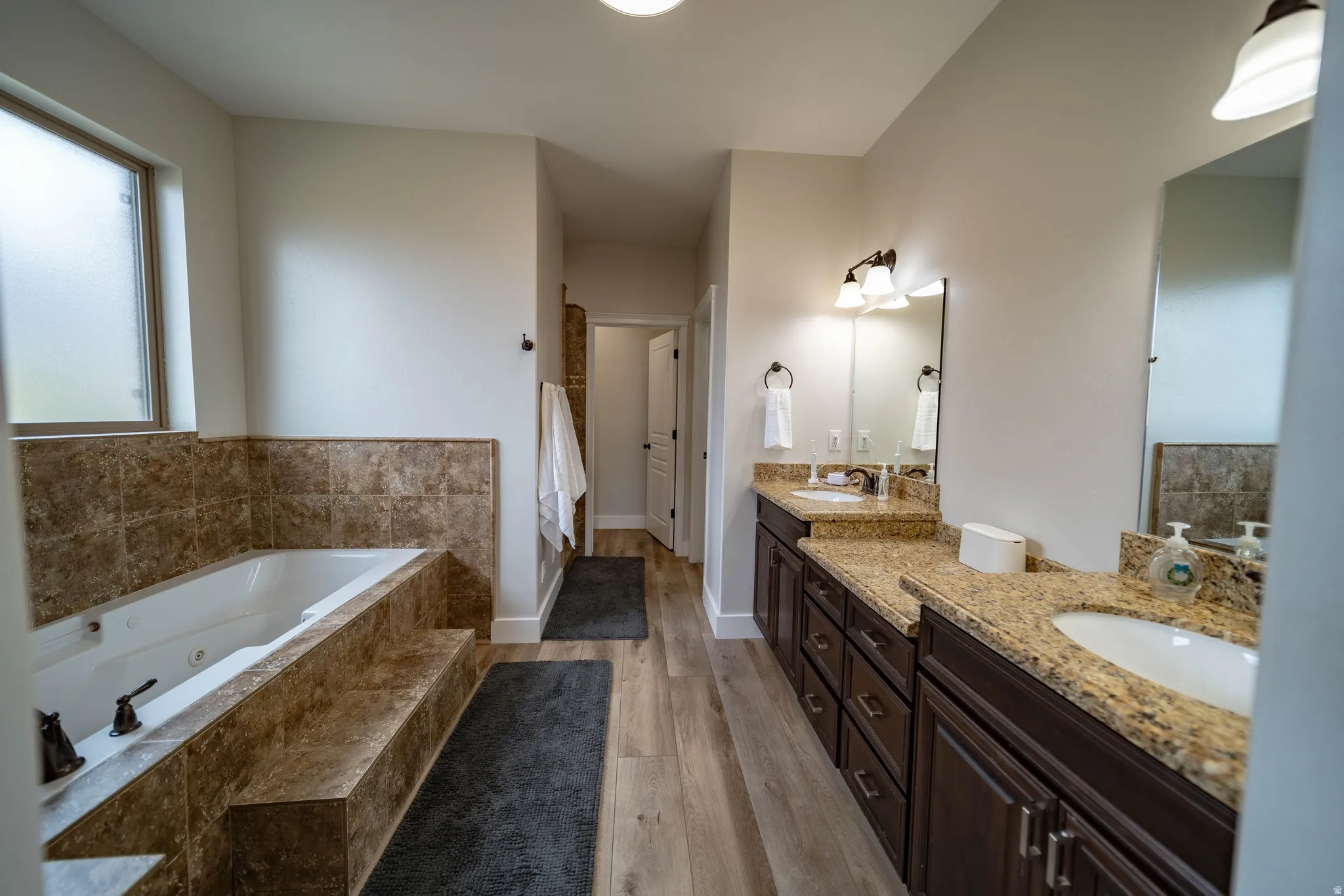 Full bath with double vanity, a whirlpool tub, light wood-style floors, and a walk in shower