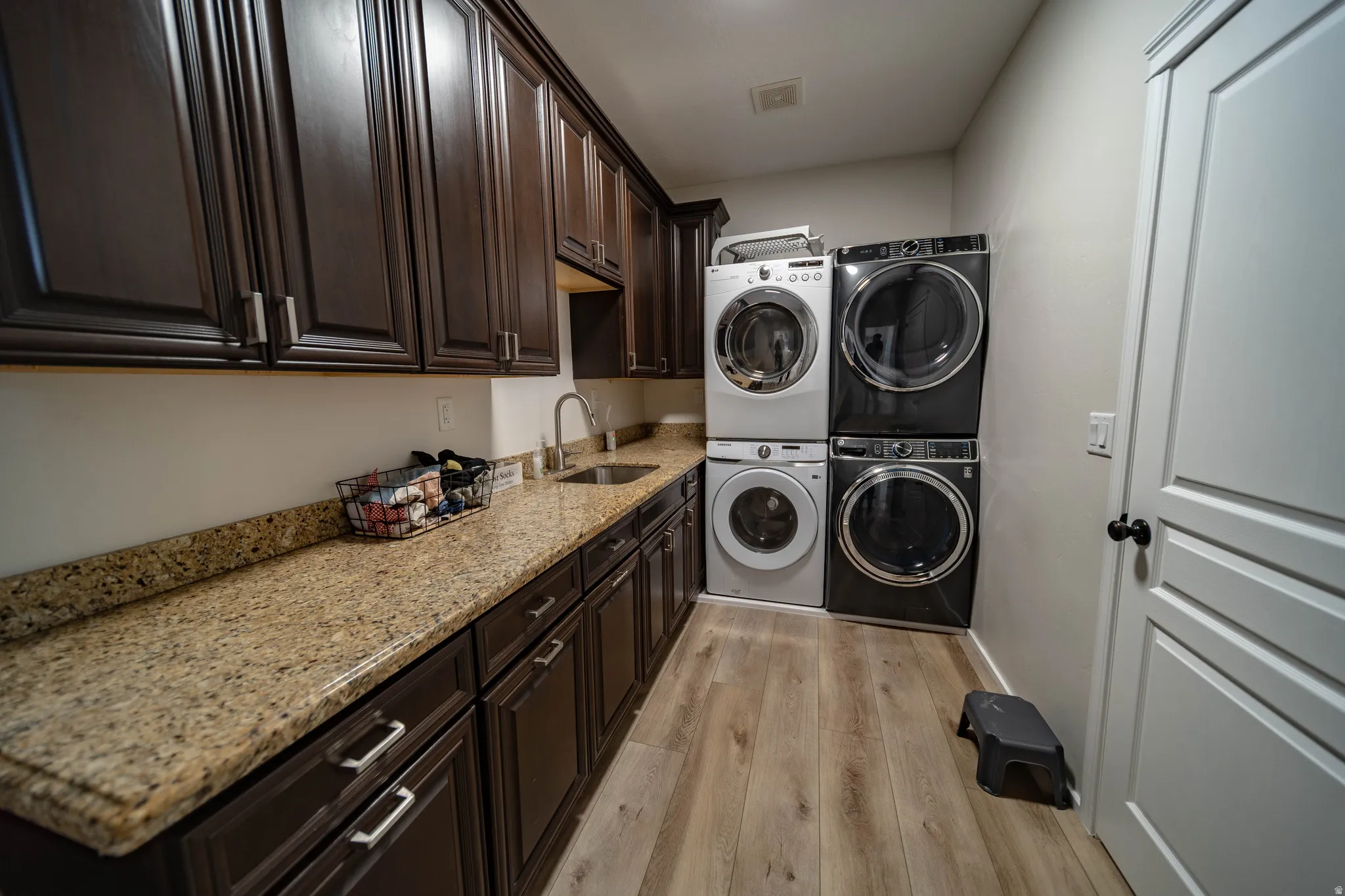 Laundry room featuring light wood-type flooring, stacked washer and dryer, and cabinet space