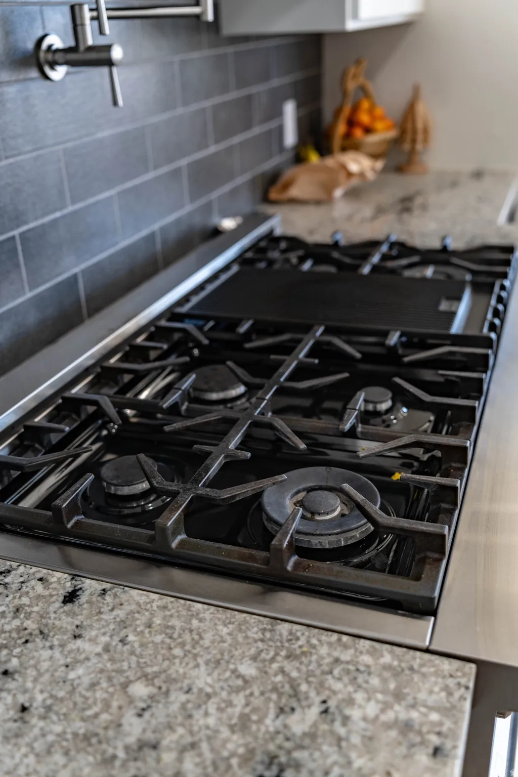 Kitchen view of decorative backsplash, stainless steel gas cooktop, and light stone counters