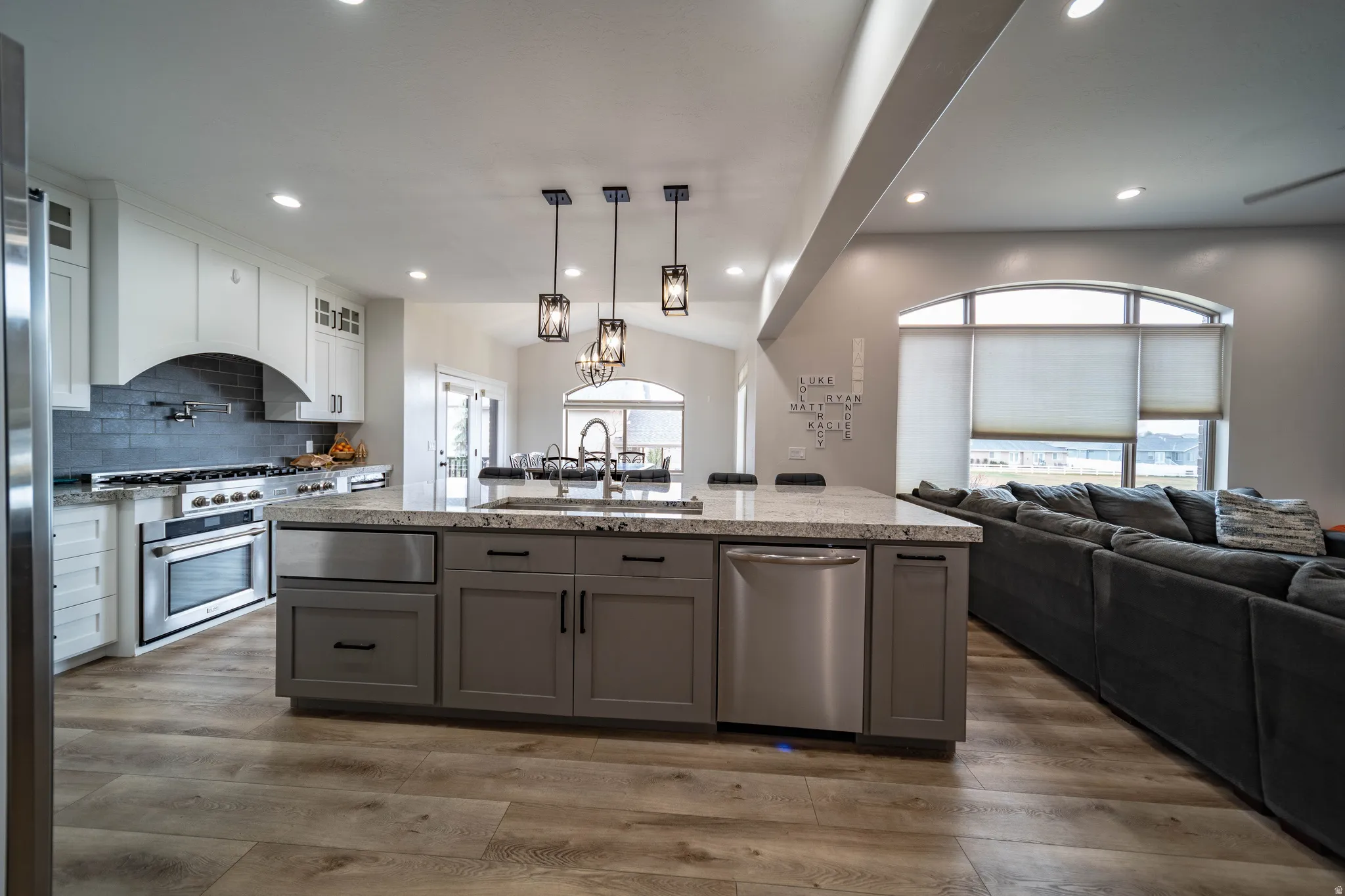 Dual tone kitchen with open floor plan, stainless steel appliances, a kitchen island with sink, dual tone cabinets, and light stone counters