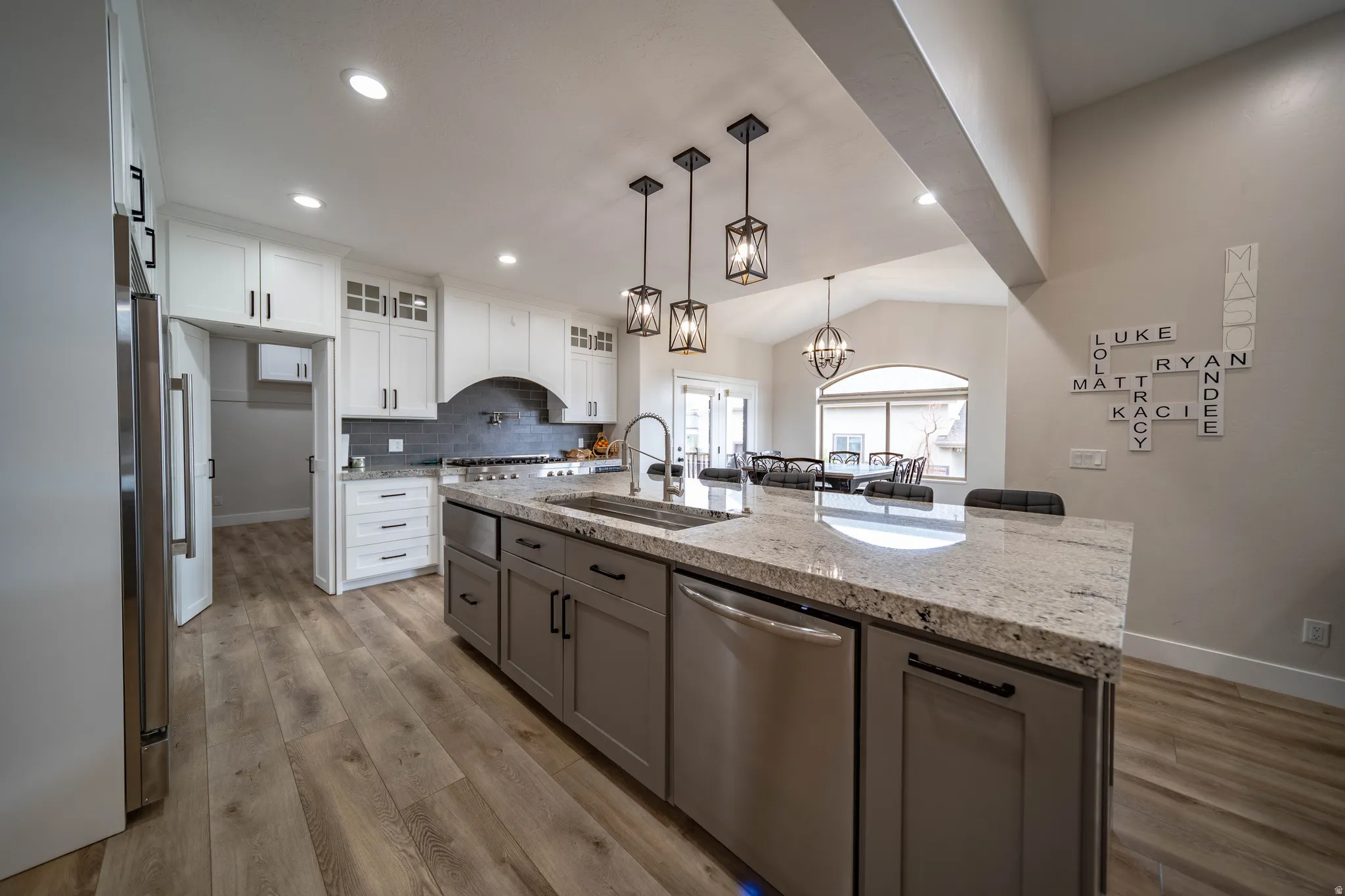 Kitchen featuring glass insert cabinets, vaulted ceiling, a center island with sink, stainless steel appliances, and light wood-style floors