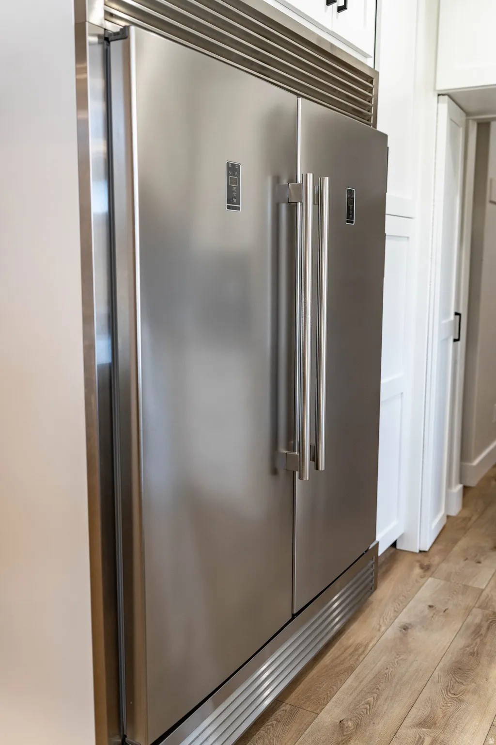 Kitchen view of light wood-type flooring and built in fridge