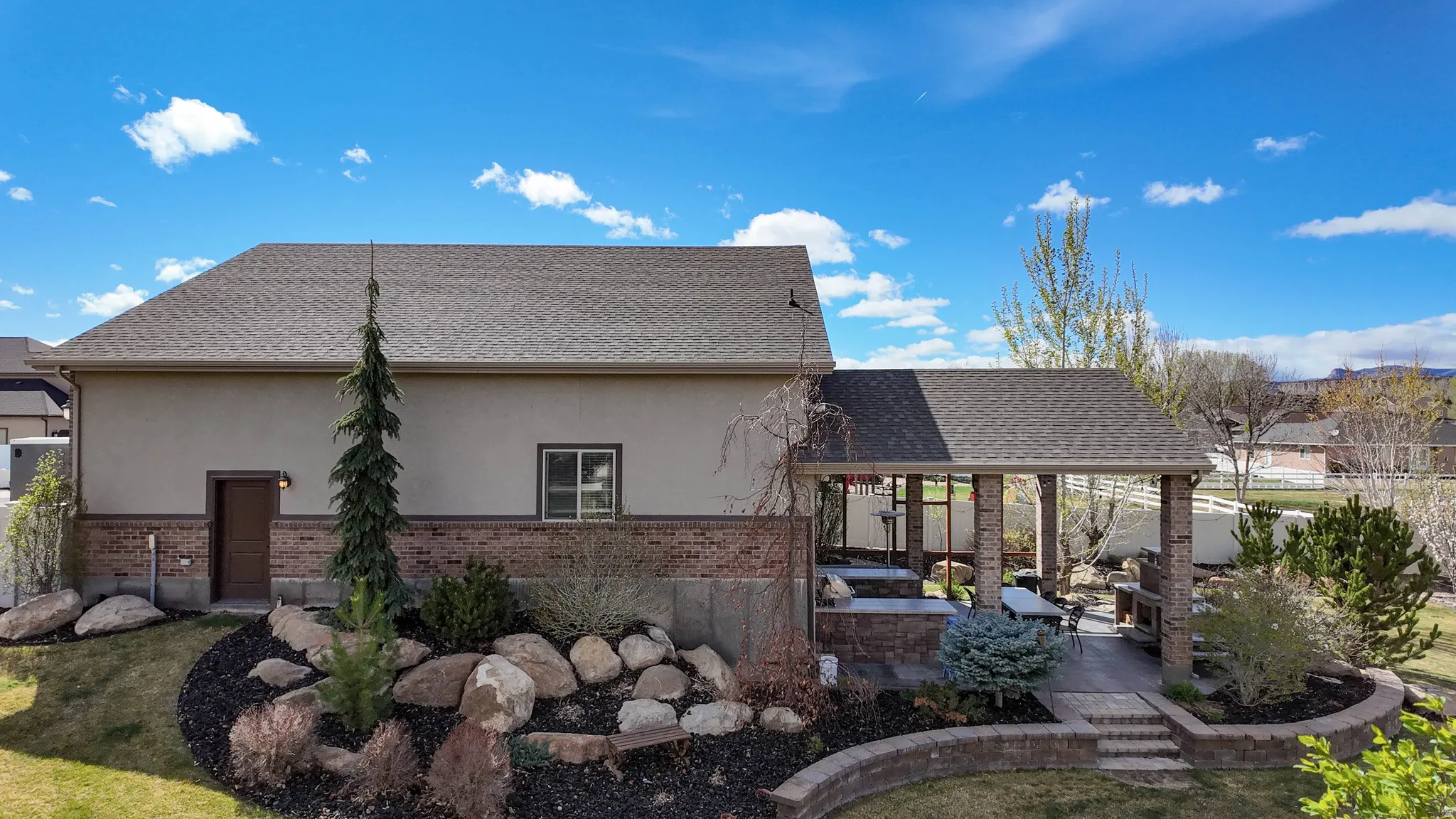 Back of property with brick siding, stucco siding, a patio, and roof with shingles