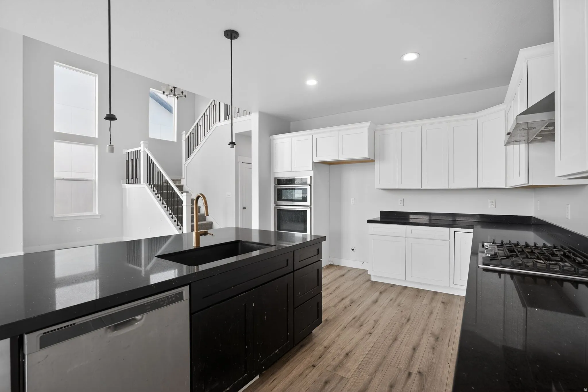 Two tone kitchen featuring stainless steel appliances, dual tone cabinetry, light wood-type flooring, dark stone counters, and pendant lighting
