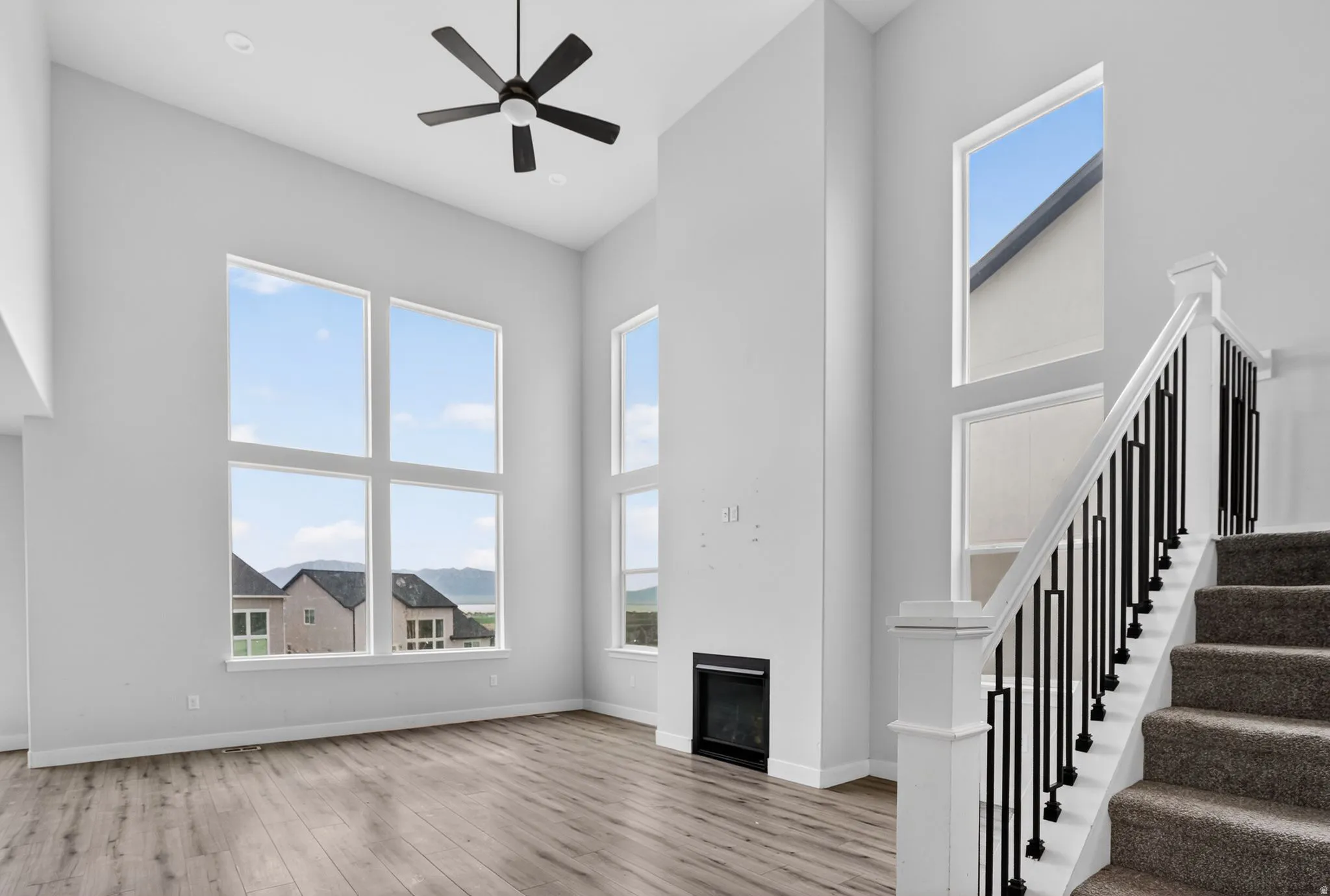 Unfurnished living room featuring a high ceiling, a glass covered fireplace, light wood-style floors, and ceiling fan