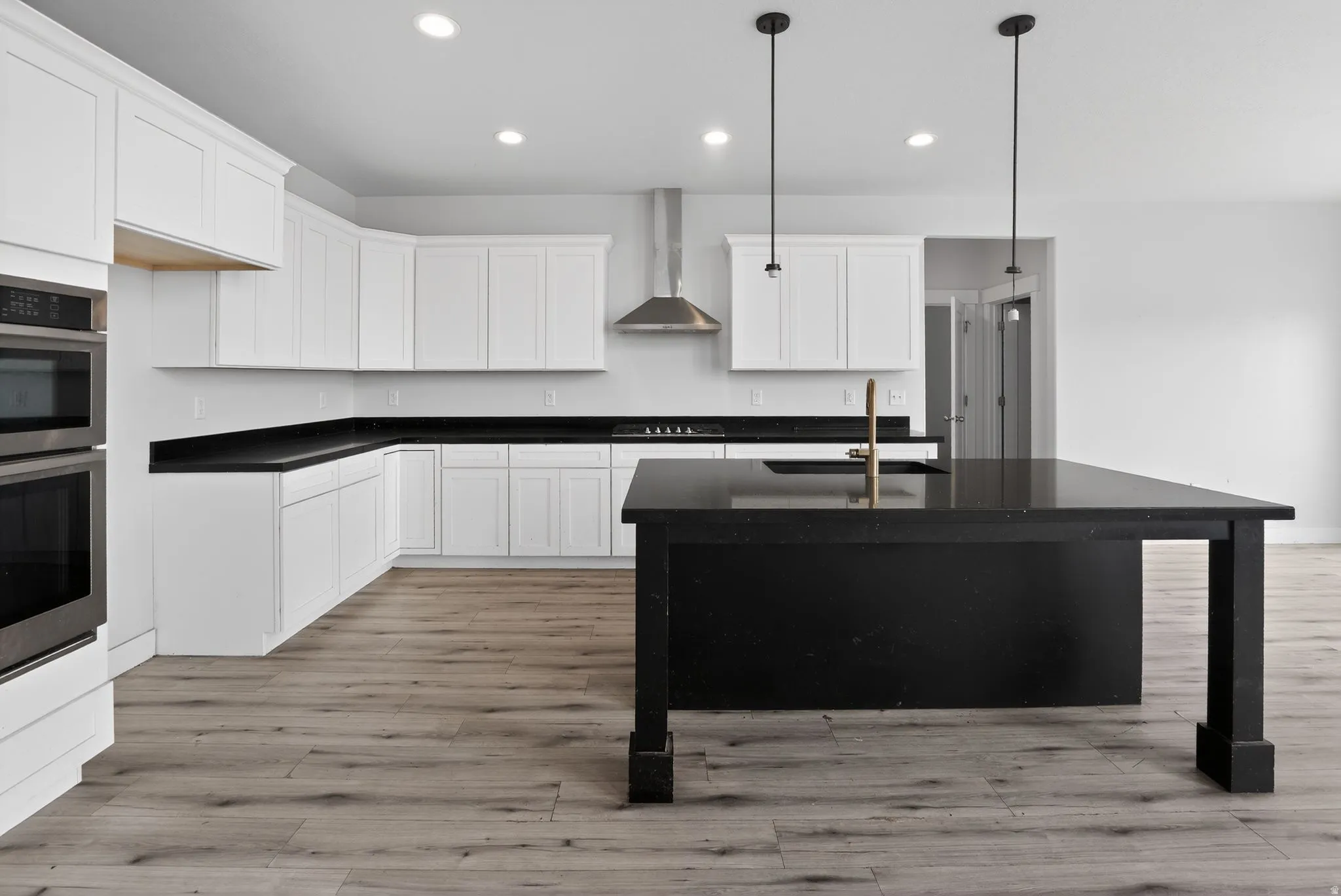 Kitchen with white cabinetry, a center island with sink, stainless steel double oven, and light wood-style floors
