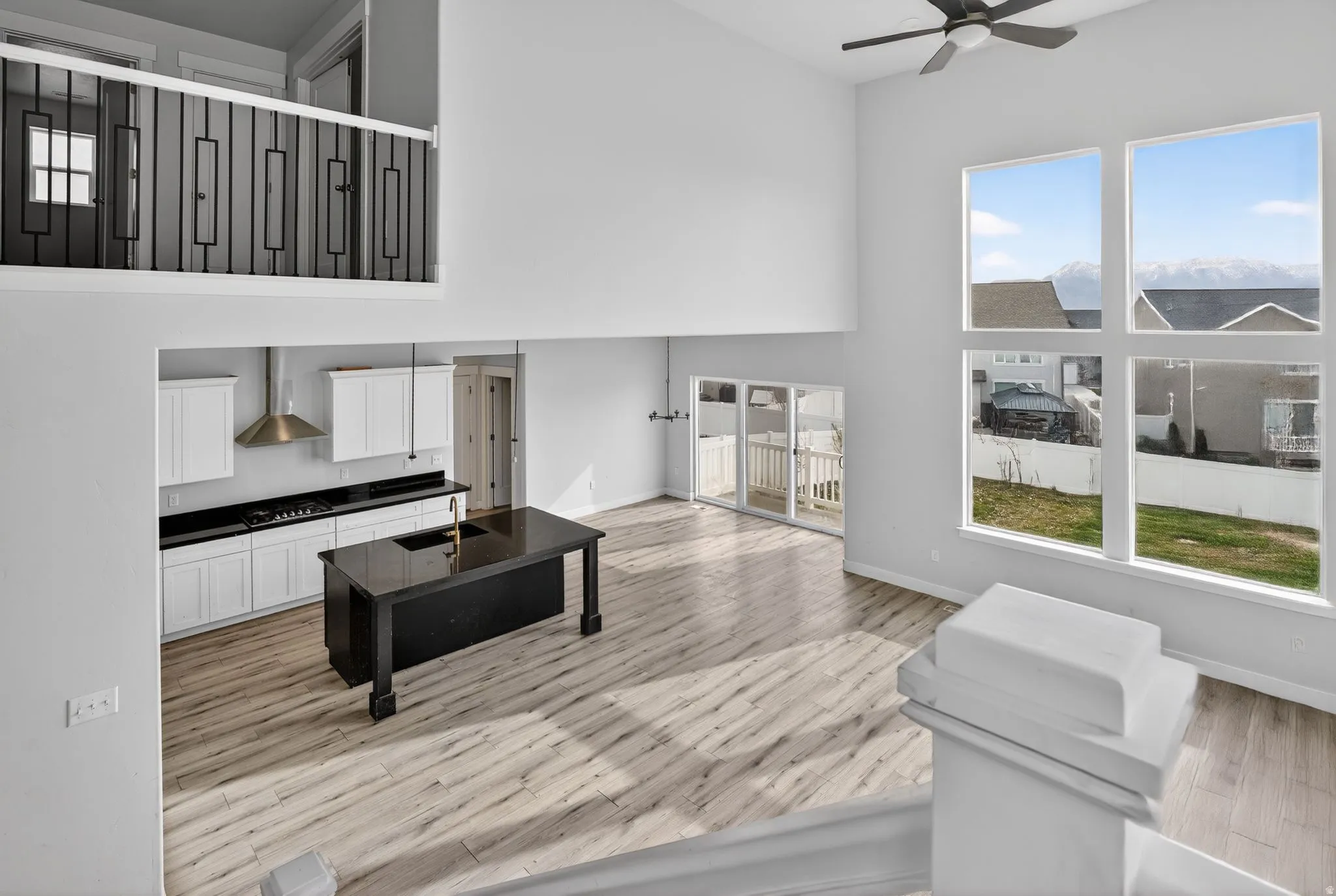Living room with a high ceiling, plenty of natural light, ceiling fan, and light wood-style floors