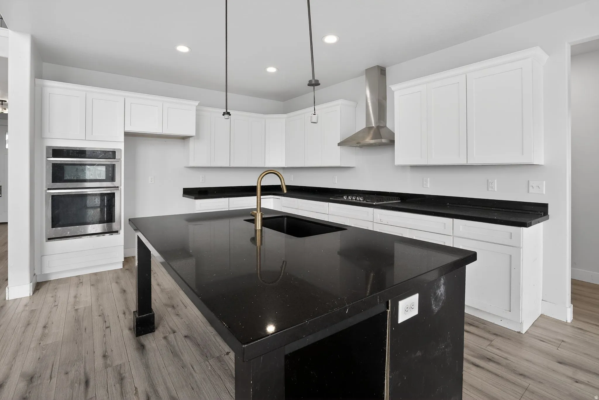 Kitchen featuring a kitchen island with sink, white cabinets, stainless steel appliances, and light wood-style flooring