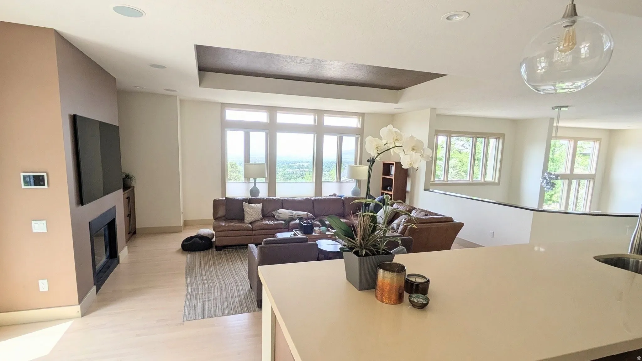 Open-concept living area with light wood-finish flooring, a contemporary fireplace, recessed lighting, and large windows providing ample illumination and valley views.
