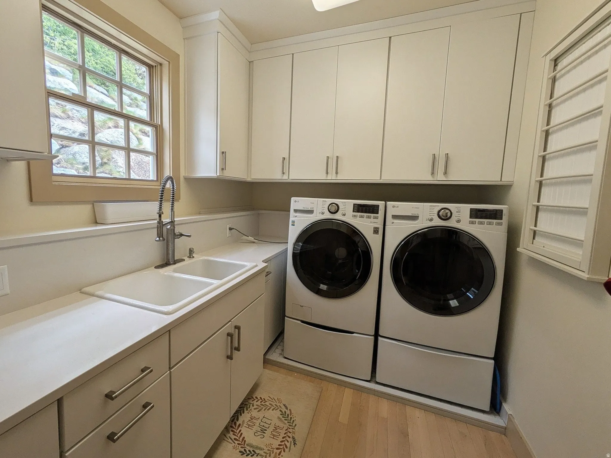 Laundry room featuring white cabinetry, a double basin sink with a gooseneck faucet, light countertops, and wood-finish flooring, drying rack and fold up ironing board