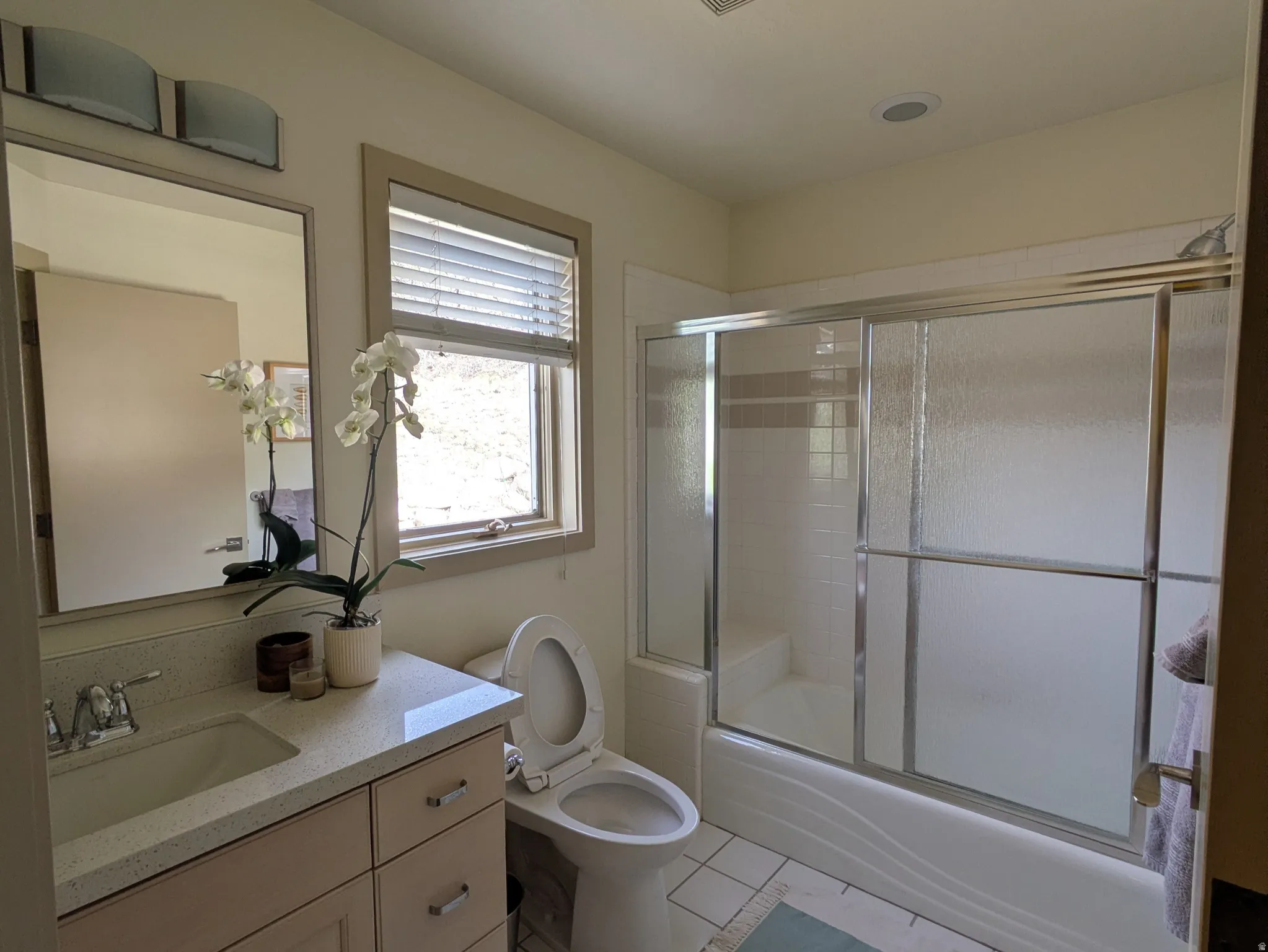 Full ensuite bathroom featuring vanity, shower / bath combination with glass door, and light tile patterned flooring
