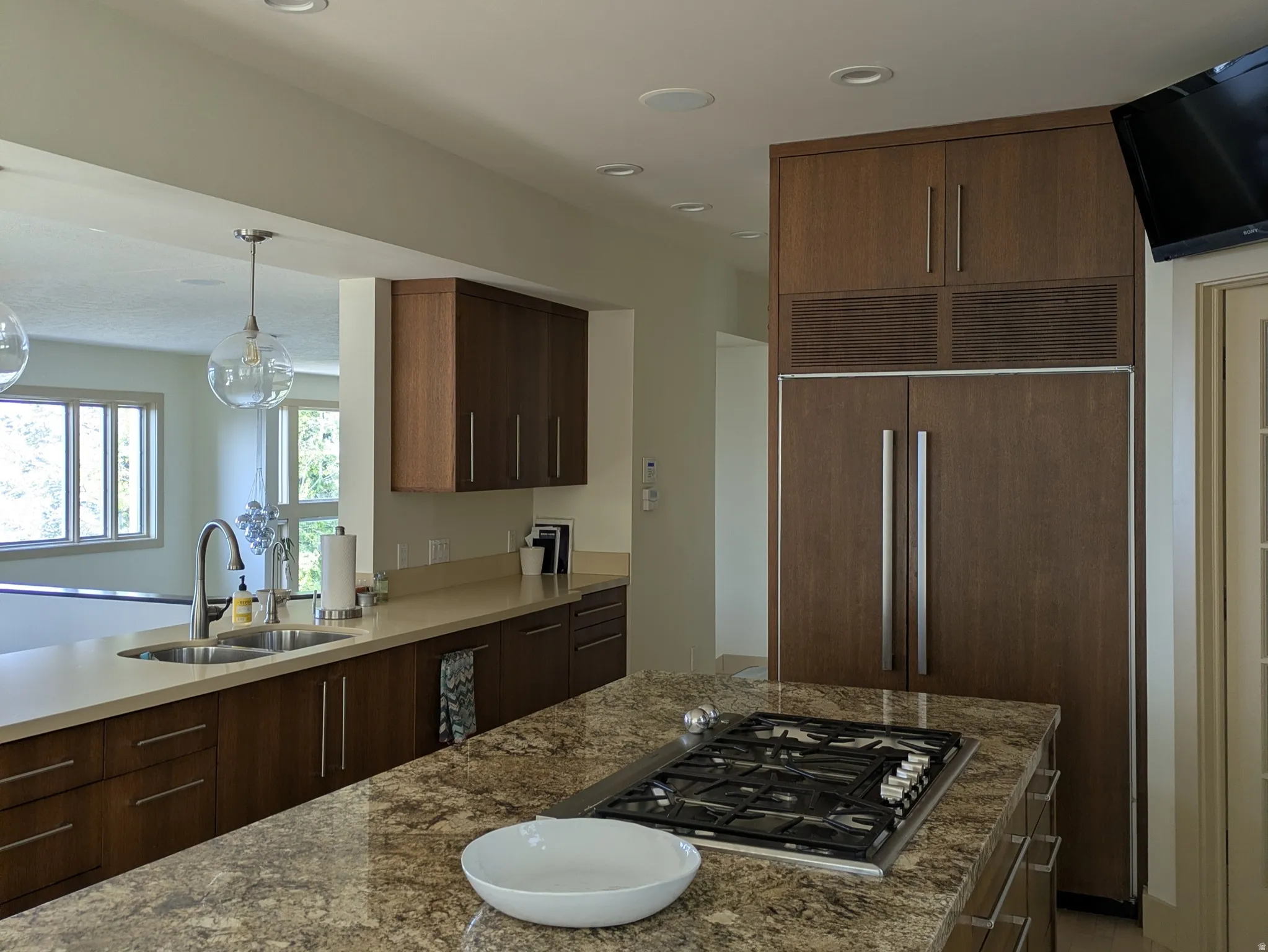 Kitchen featuring paneled built in fridge, stainless steel gas stovetop, light stone countertops, light wood finished floors, and a center island, open to family room