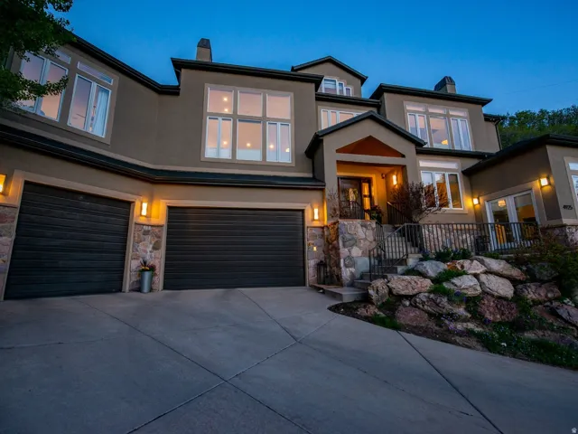 View of front of house with a chimney, stucco siding, driveway, an attached garage, and stone siding