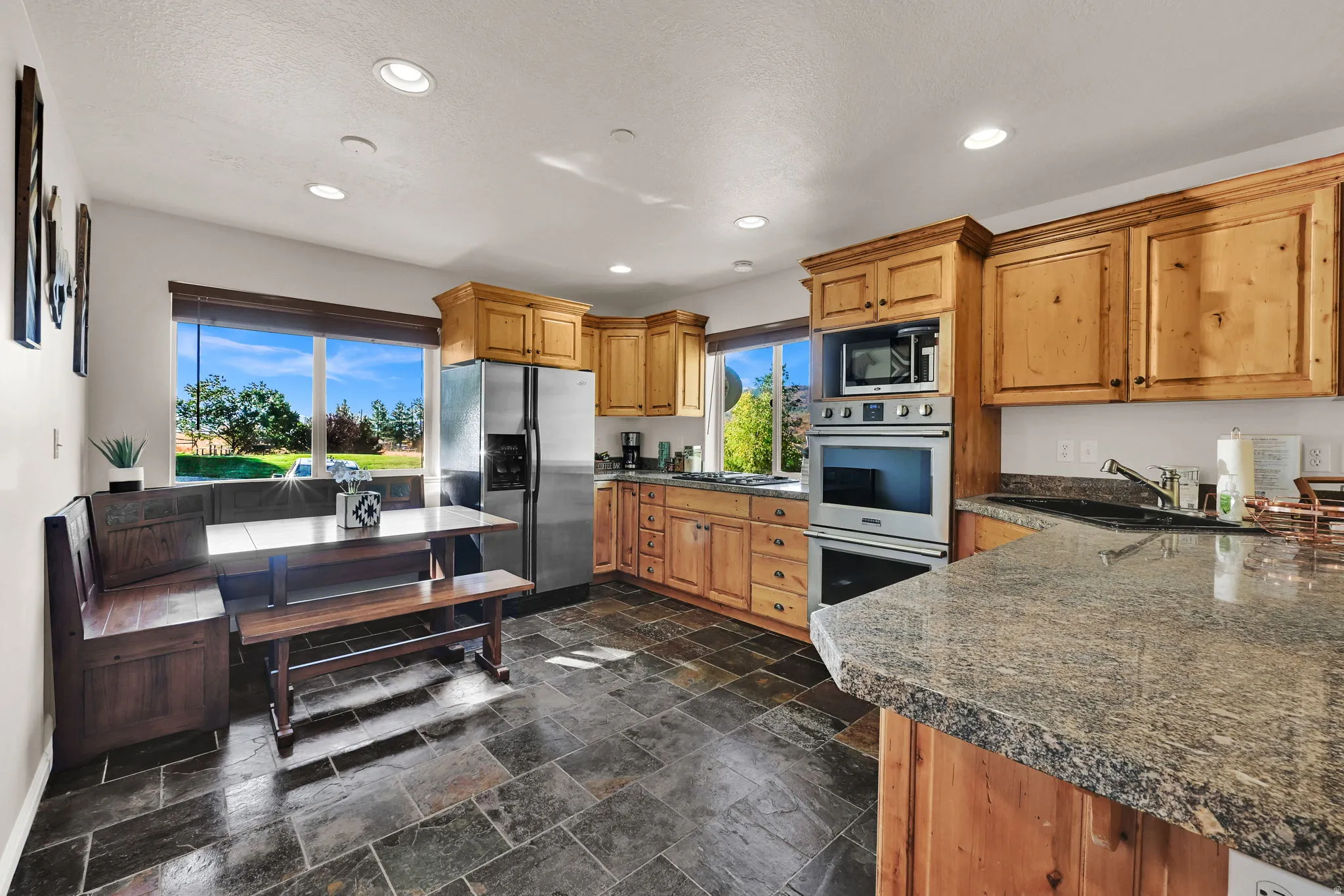 Kitchen featuring stainless steel appliances, stone tile floors, recessed lighting, wood finish cabinets, and dark stone countertops