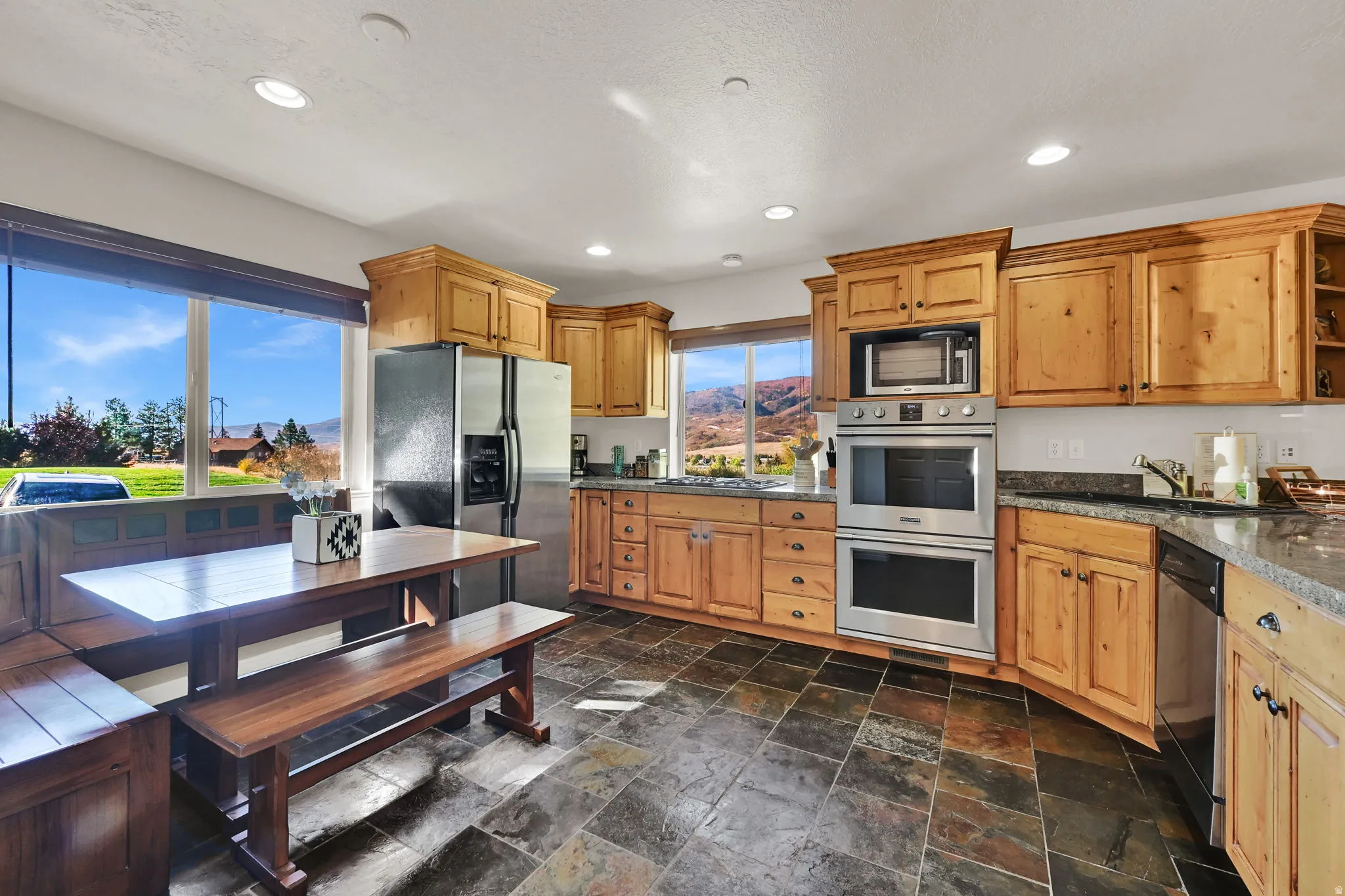 Kitchen featuring stainless steel appliances, stone tile flooring, recessed lighting, wood finish cabinetry, and dark stone countertops