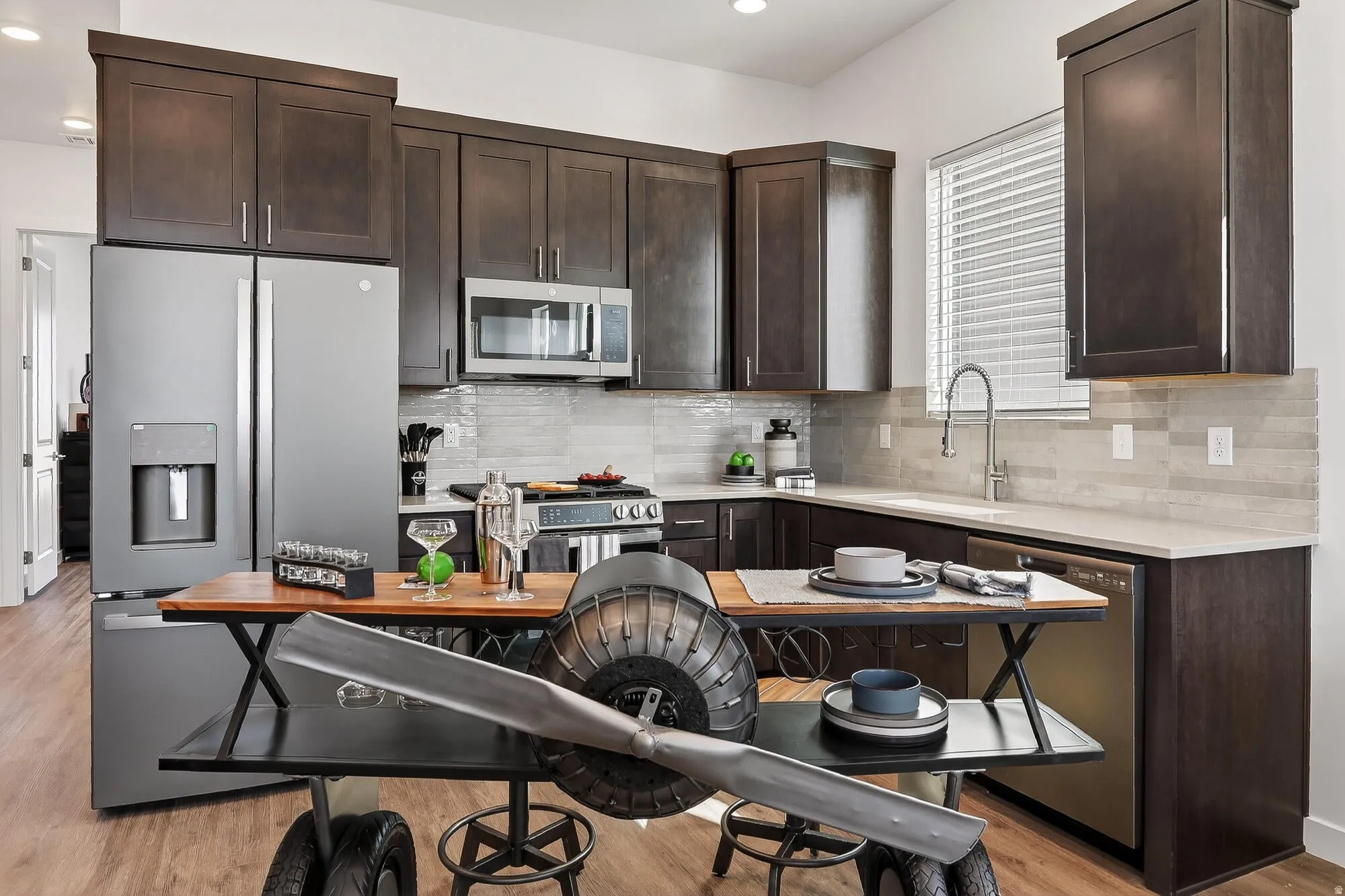 Kitchen with dark wood finish cabinets, stainless steel appliances, light wood-style floors, decorative backsplash, and recessed lighting