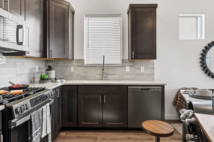 Kitchen featuring stainless steel appliances, dark wood finish cabinetry, light stone counters, light wood-type flooring, and decorative backsplash