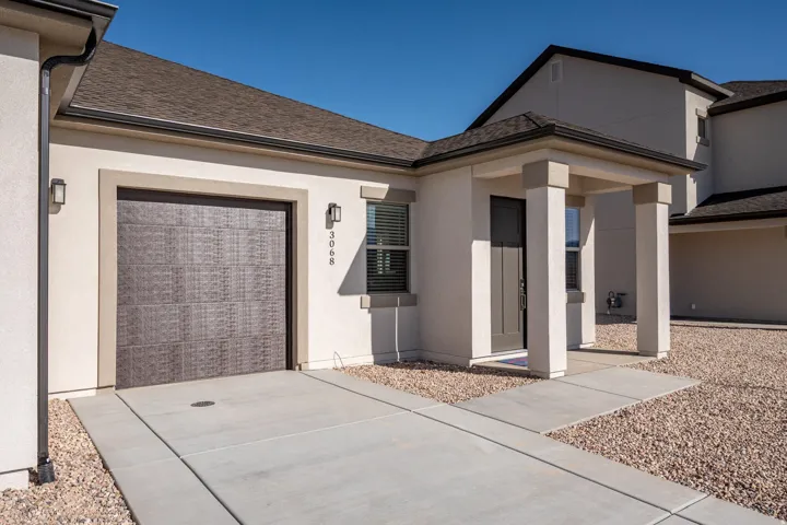 Doorway to property with a garage, stucco siding, driveway, and roof with shingles