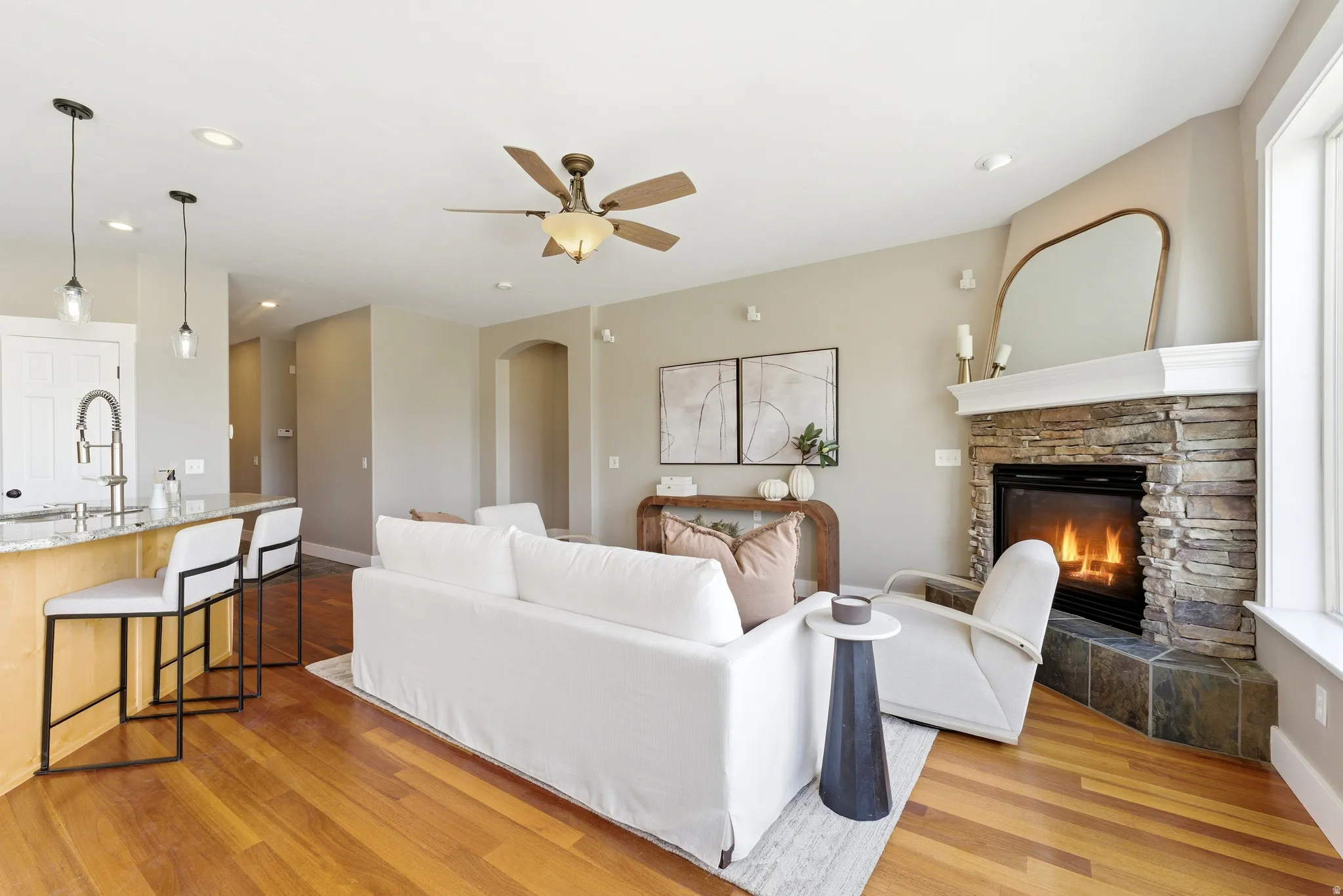 Living room featuring ceiling fan, arched walkways, light wood-style flooring, a fireplace, and recessed lighting