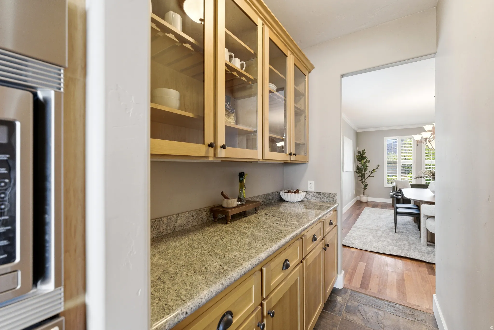 Bar area featuring glass fronted cabinets, stainless steel microwave, light stone countertops, ornamental molding, and dark wood-style flooring