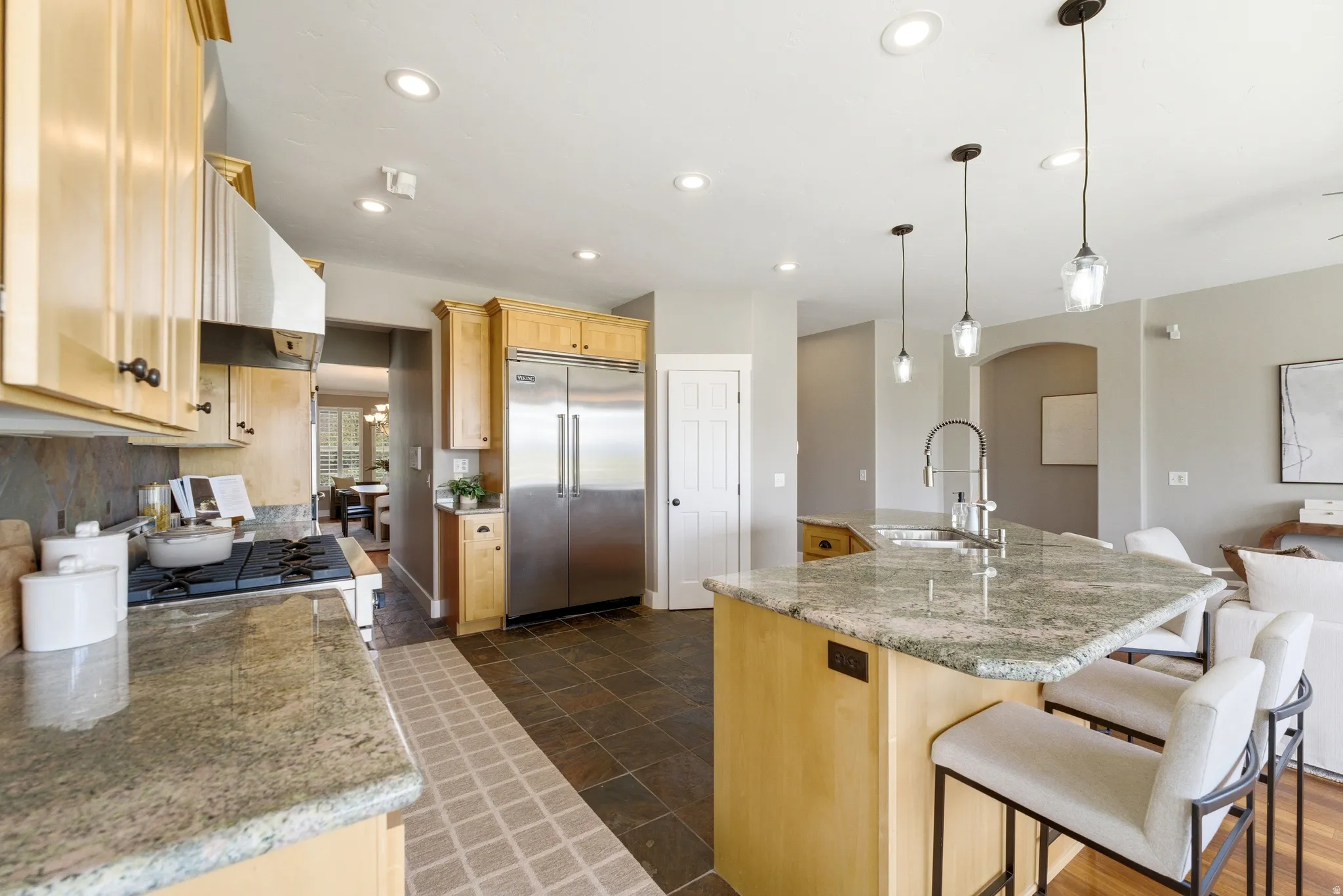 Kitchen with light wood finish cabinets, stainless steel appliances, a large island, a breakfast bar area, and light stone counters