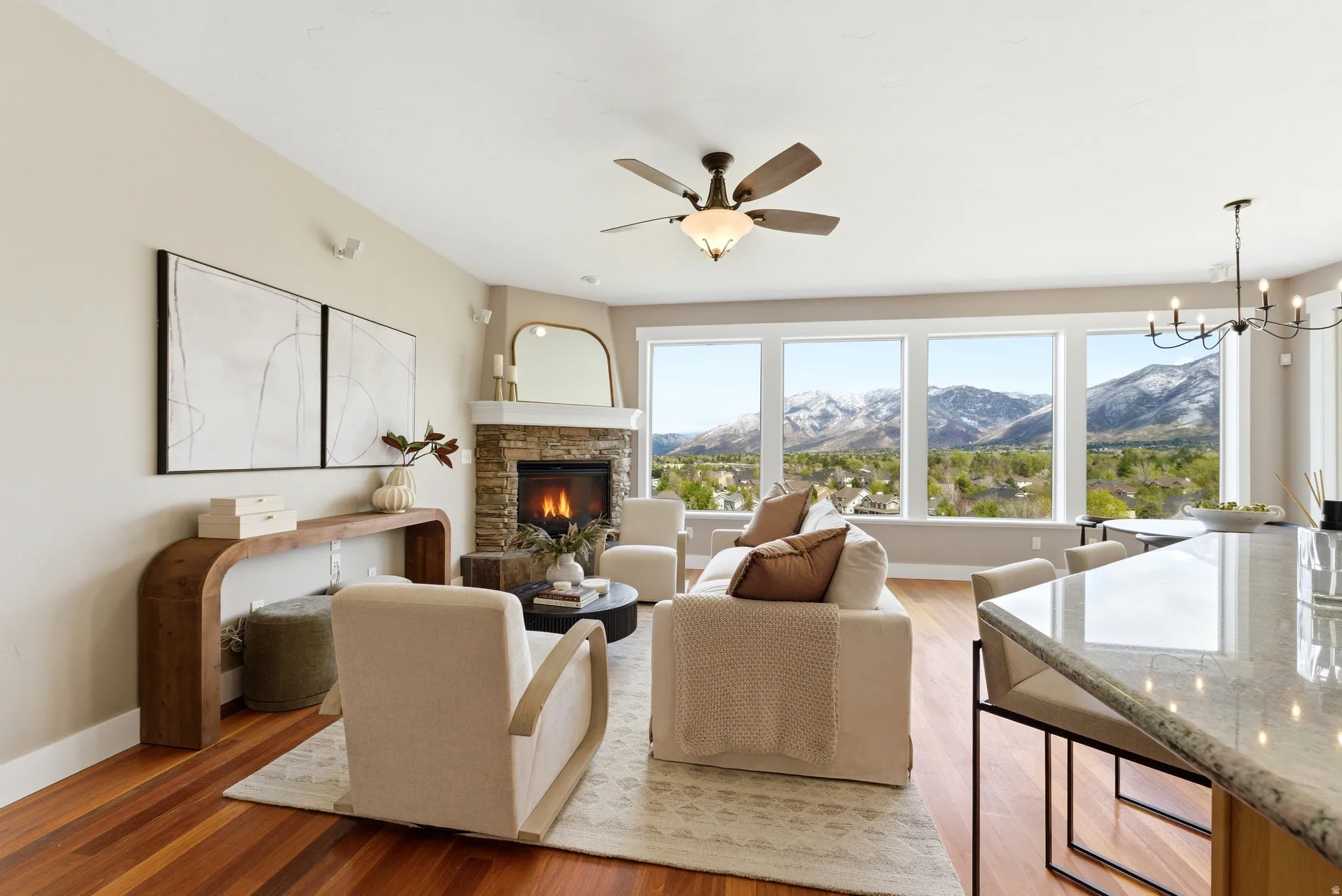 Living area with a mountain view, light wood-style flooring, a stone fireplace, ceiling fan, and suspended lighting