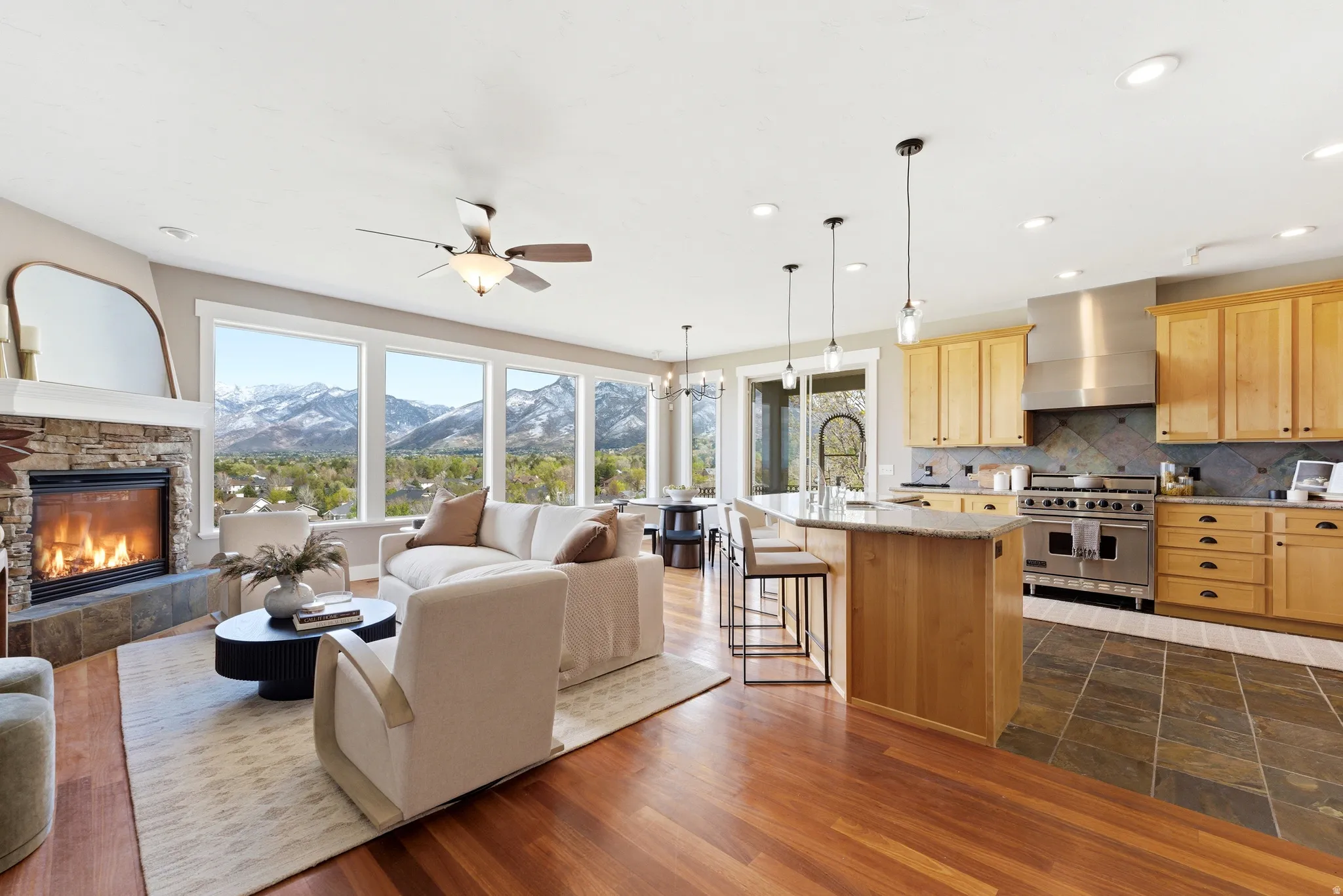 Living room with a stone fireplace, a mountain view, hanging lights, a ceiling fan, and dark wood-style flooring