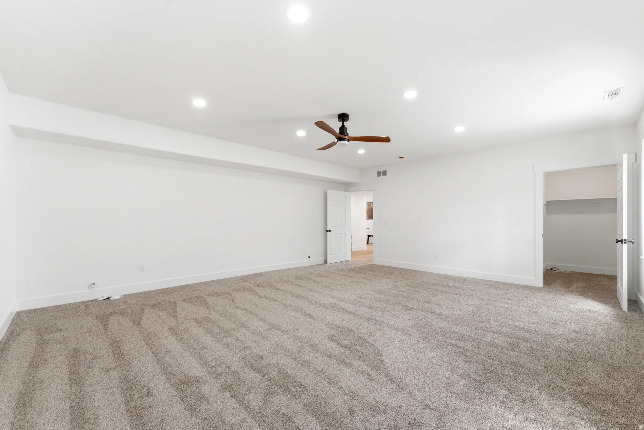 Bedroom featuring light colored carpet, recessed lighting, walk in closet, and ceiling fan