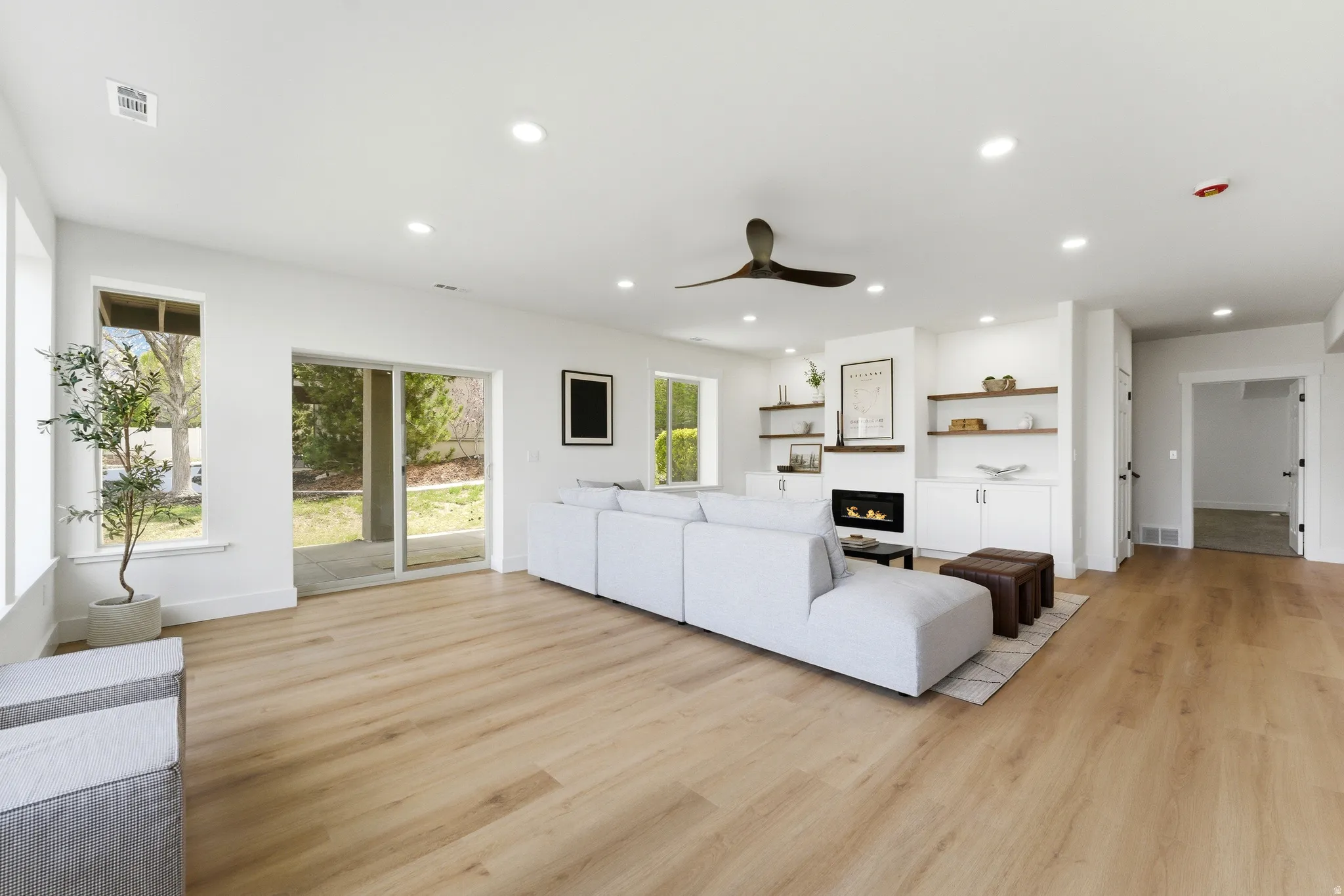Living room featuring a ceiling fan, light wood-type flooring, a glass covered fireplace, and recessed lighting