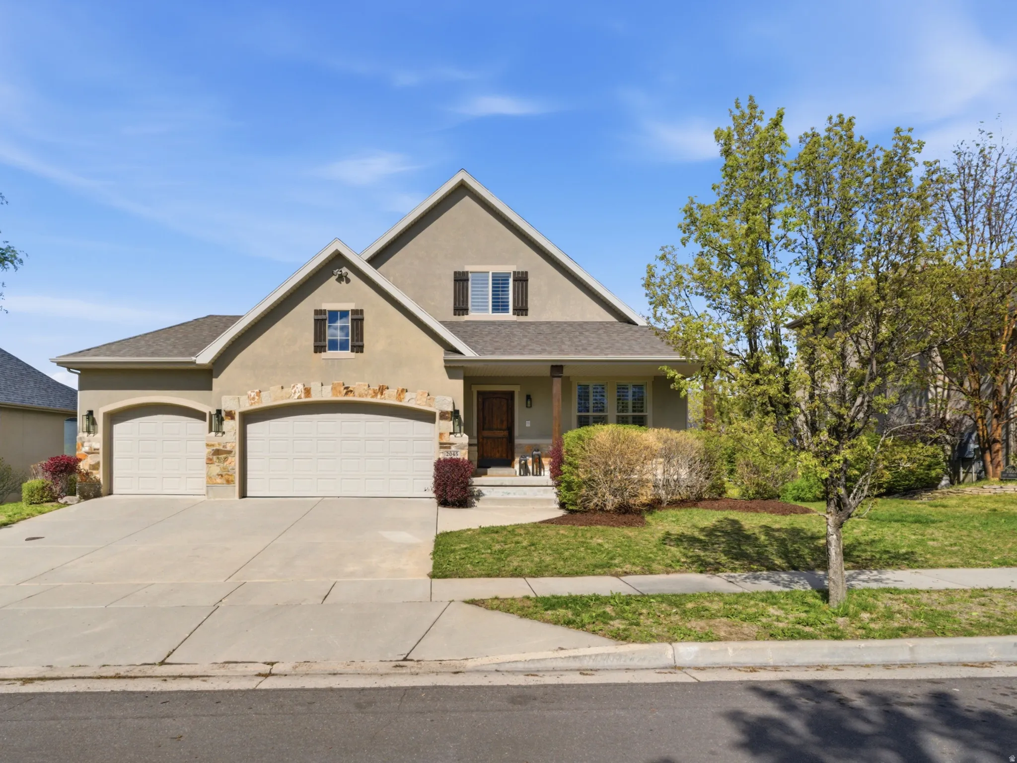 Traditional-style house with a porch, a front lawn, concrete driveway, stucco siding, and an attached 3 car garage