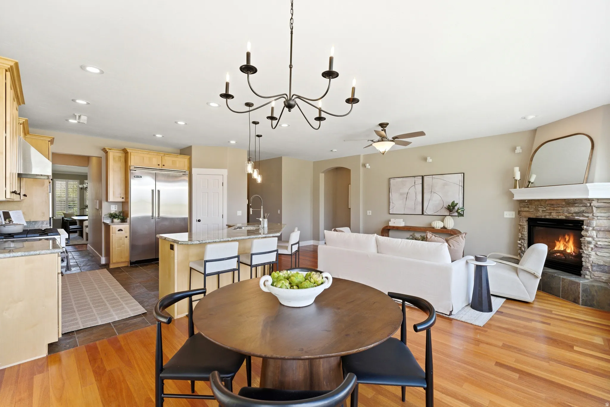 Dining area featuring a ceiling fan, arched walkways, suspended lighting, a stone fireplace, and dark wood finished floors